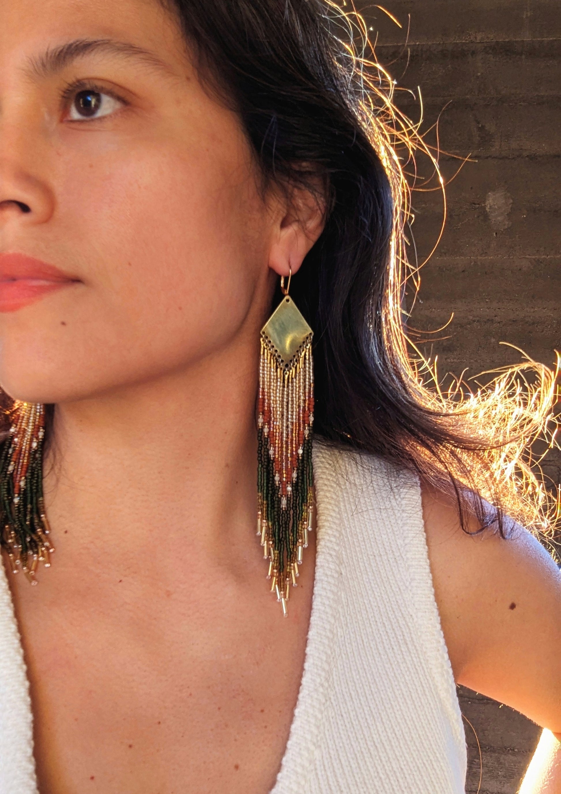 Seed bead earrings with an elegant, geometric design and beaded fringe in warm earth tones, worn by a woman in soft lighting, highlighting the intricate detail and shimmer of the beads.- Moon & Milk