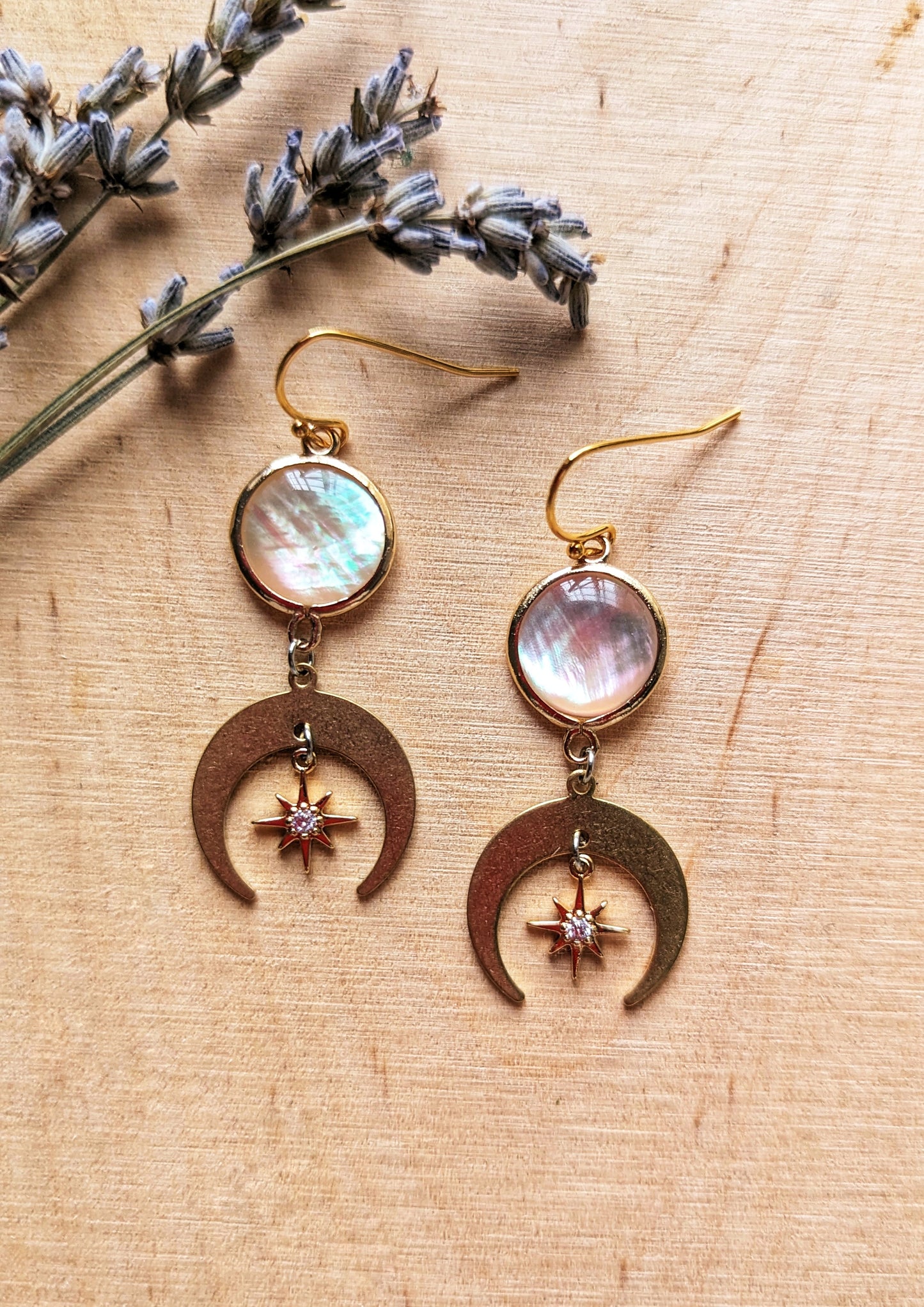 Electra MOP earrings with mother of pearl and CZ star charms, and crescent moon drops in 18k gold-plated brass on a wooden background.