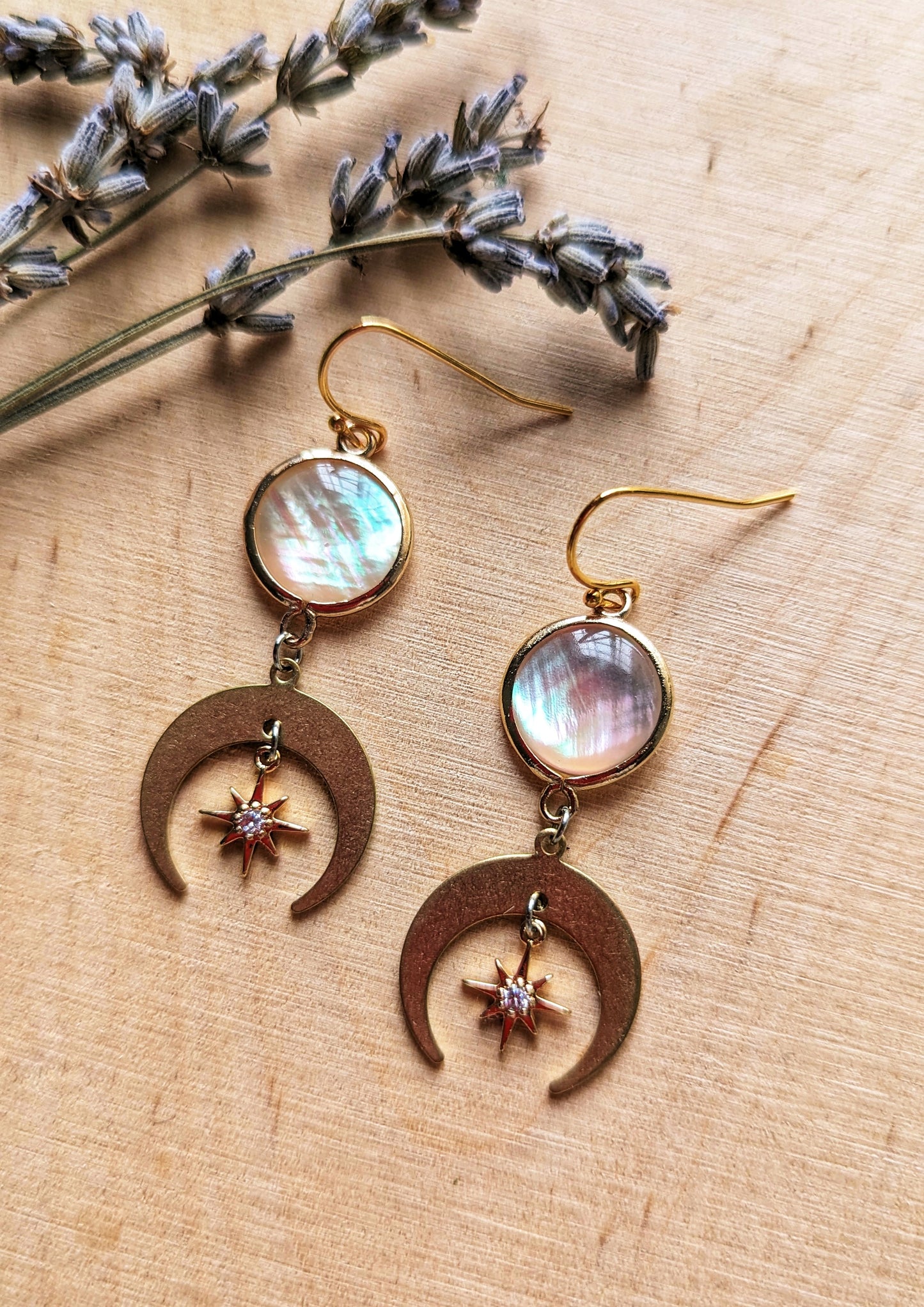 Electra MOP earrings with mother of pearl and CZ star charms, and crescent moon drops in 18k gold-plated brass on a wooden background.