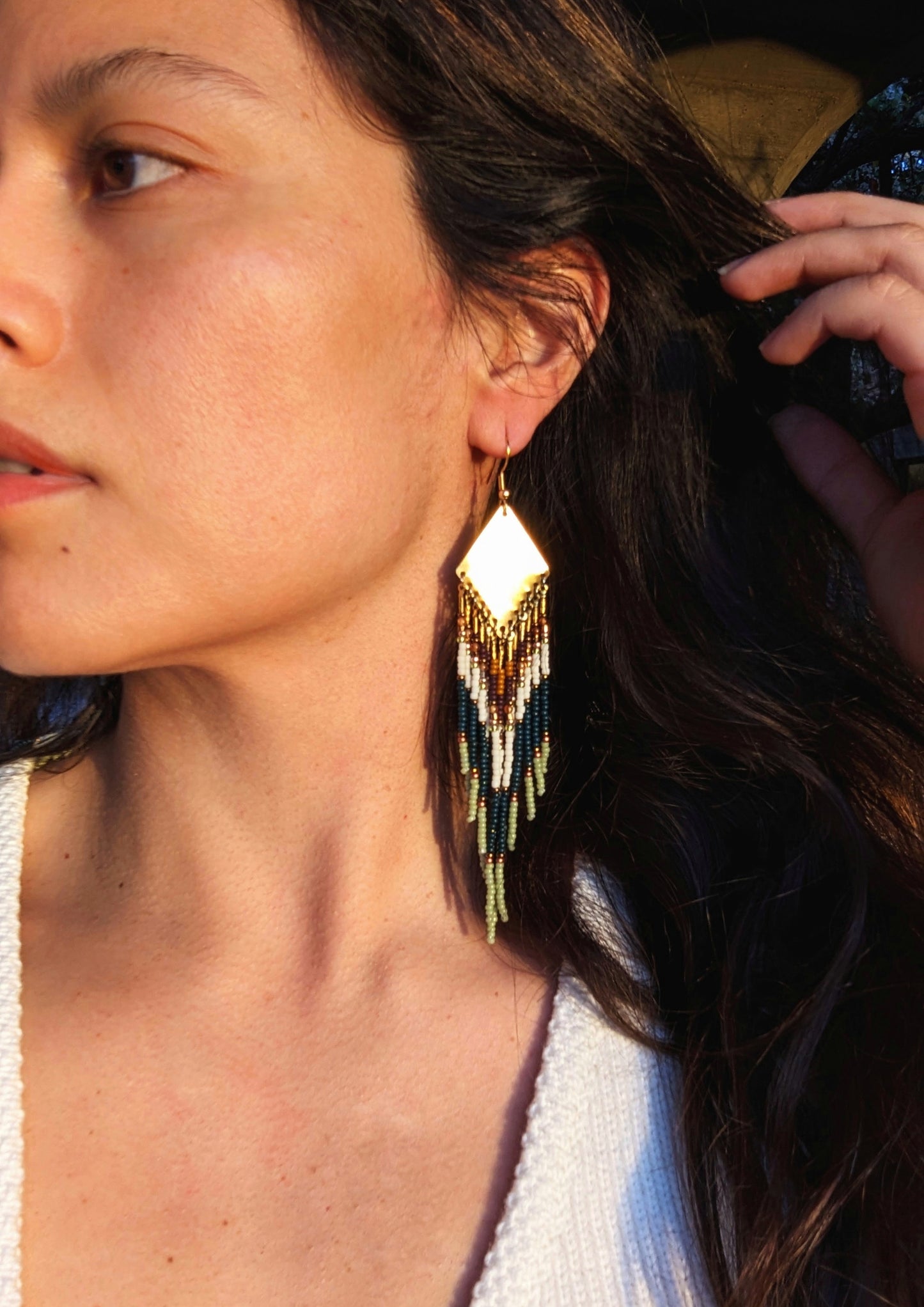 A close-up image of a woman wearing hessonite green beaded earrings with brass accents, showcasing the earrings against her skin and hair.