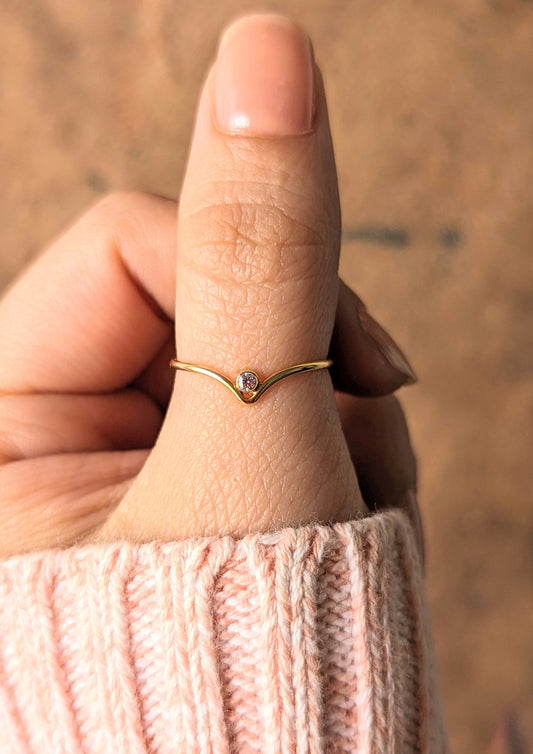 Gold filled "v" stacking ring with a tiny cubic zirconia, worn on a thumb with a pink knit sleeve.