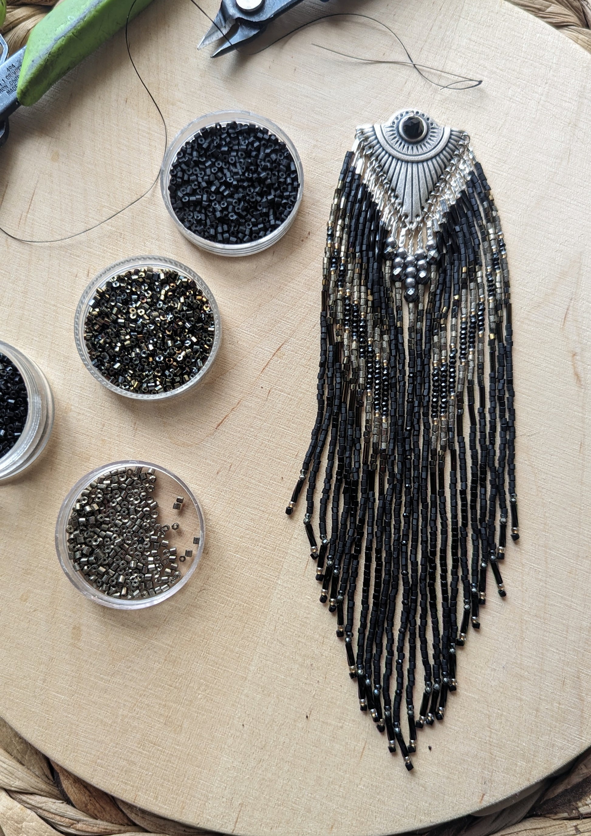 Handcrafted black beaded earrings with a fringe design. The beads feature a mix of black, silver, and gold tones, complemented by a silver fan-shaped top for an elegant, bold look