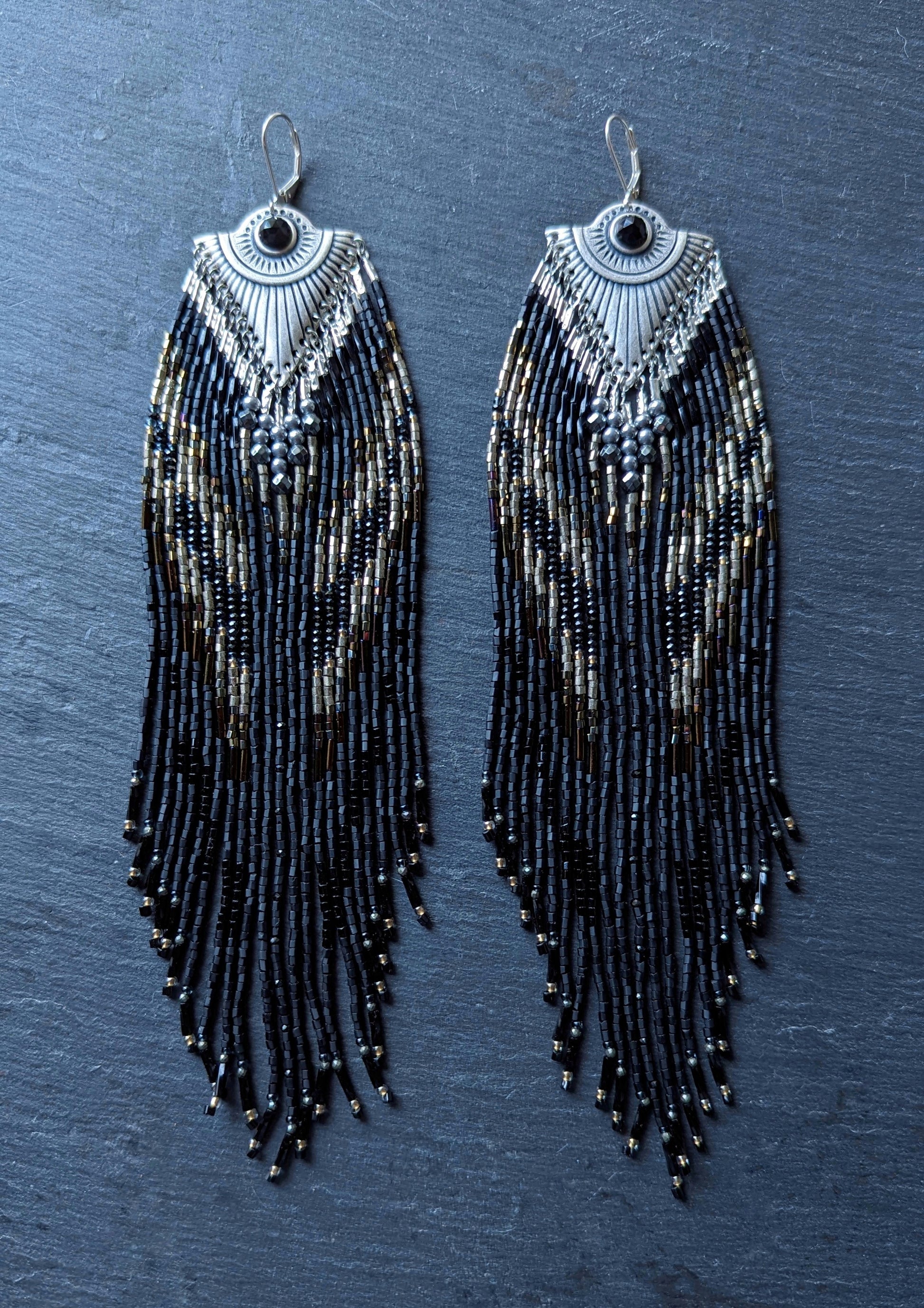 Handcrafted black beaded earrings with a fringe design. The beads feature a mix of black, silver, and gold tones, complemented by a silver fan-shaped top for an elegant, bold look
