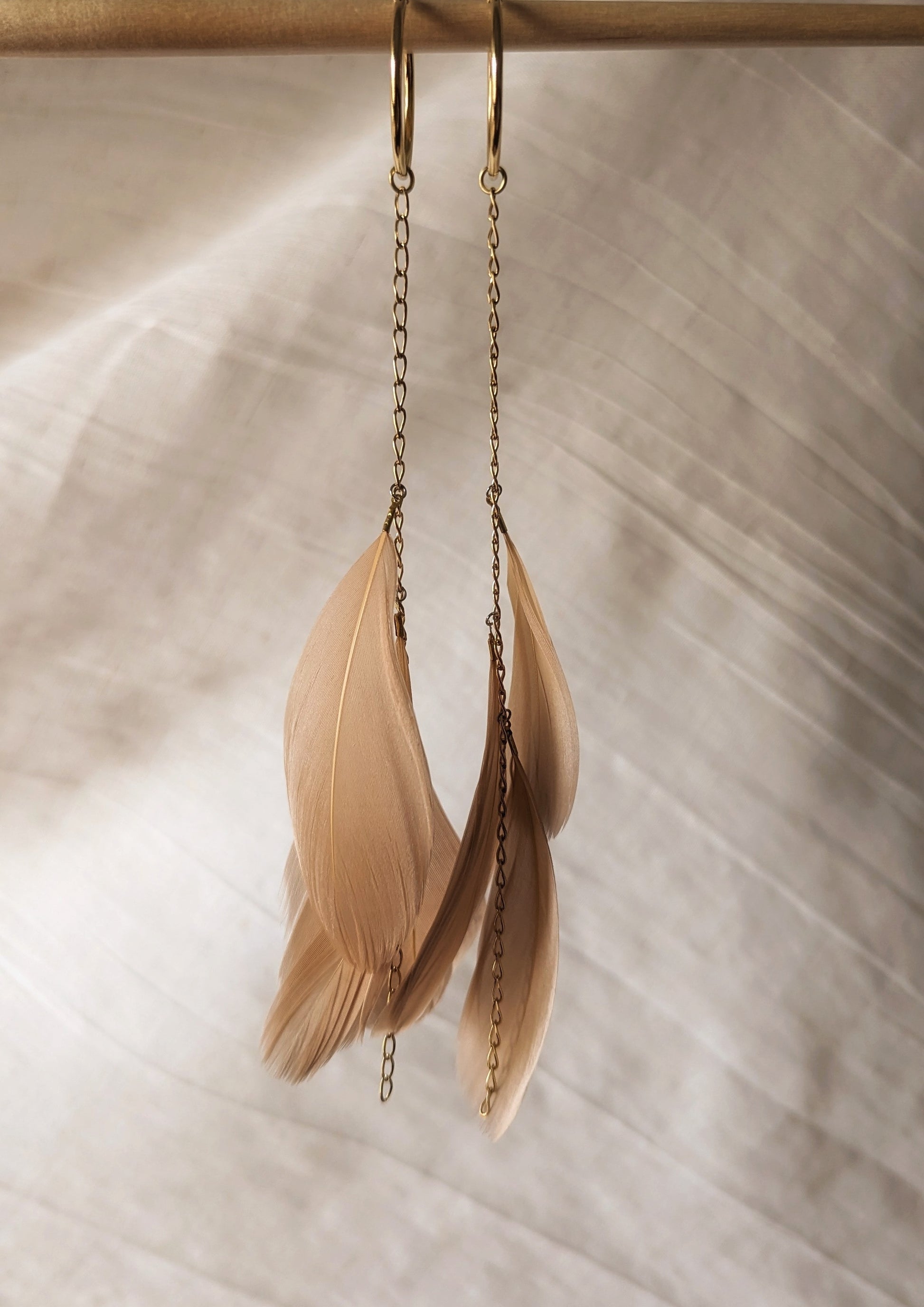Blush feather earrings with gold hoop and chain detail from Moon & Milk, hanging against a soft white fabric backdrop.