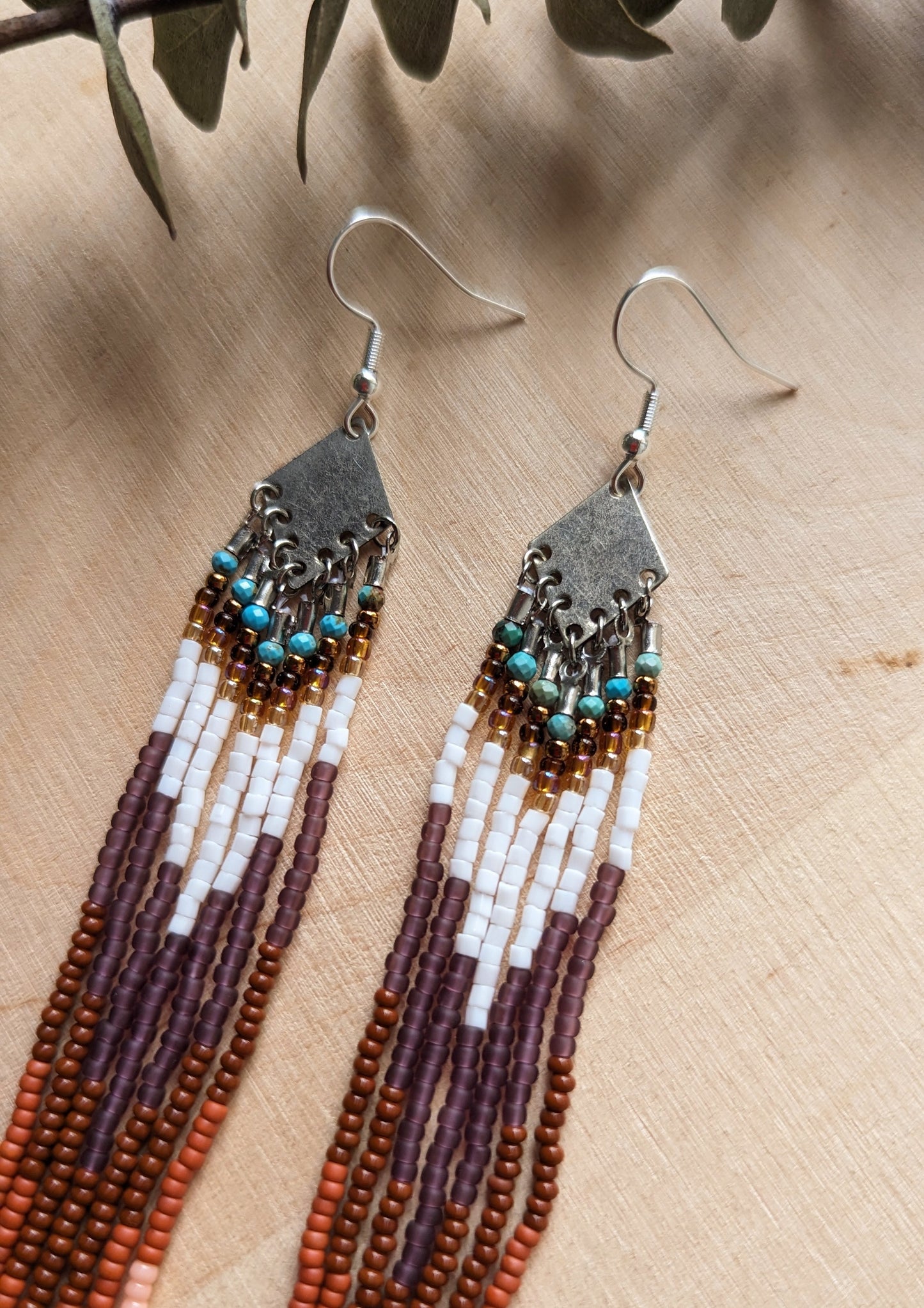 Long beaded fringe earrings with earthy tones of brown, terracotta, and white, displayed on a wooden background with dried floral accents.-Moon & Milk