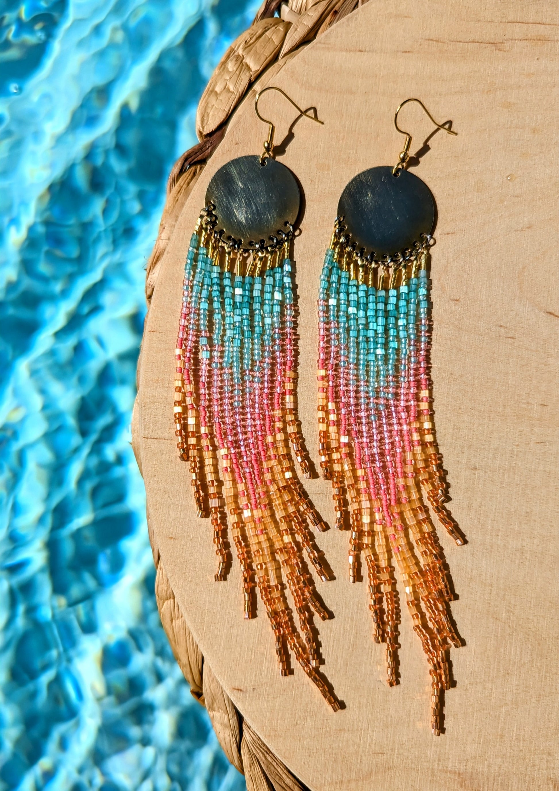 Handcrafted seed bead earrings with a vibrant ombre fringe design, transitioning from turquoise to pink to golden yellow, finished with copper-toned beads and a brass circular top.