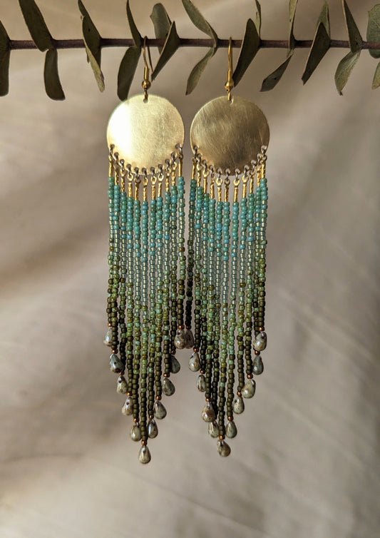 Moon & Milk long green ombré beaded earrings with brass circles and teardrop ends, handcrafted to echo forest textures and artisan beadwork style.