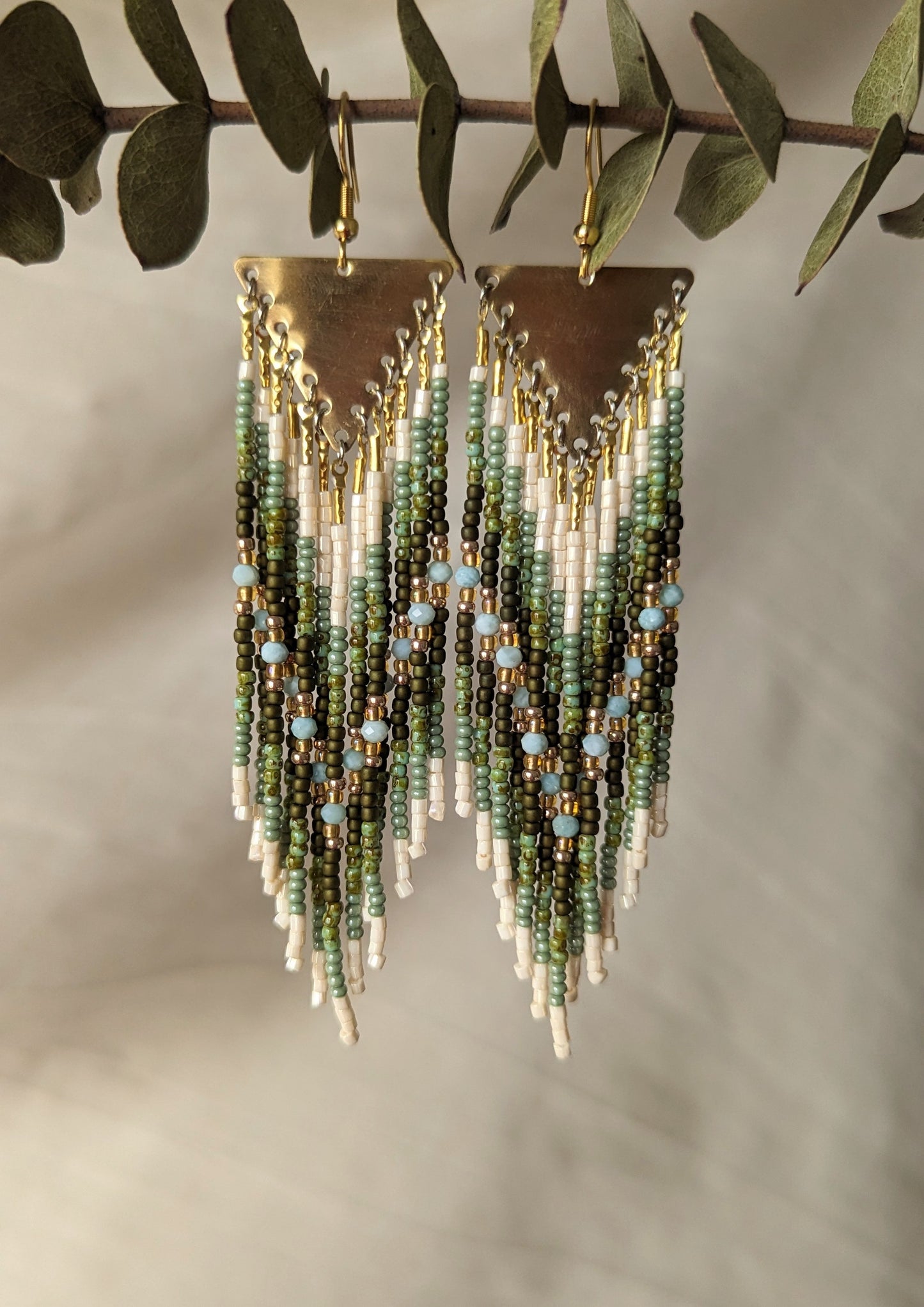 Moon & Milk green beaded earrings with ivory fringe and light blue stones, finished with brass triangles and inspired by earthy artisan beadwork.