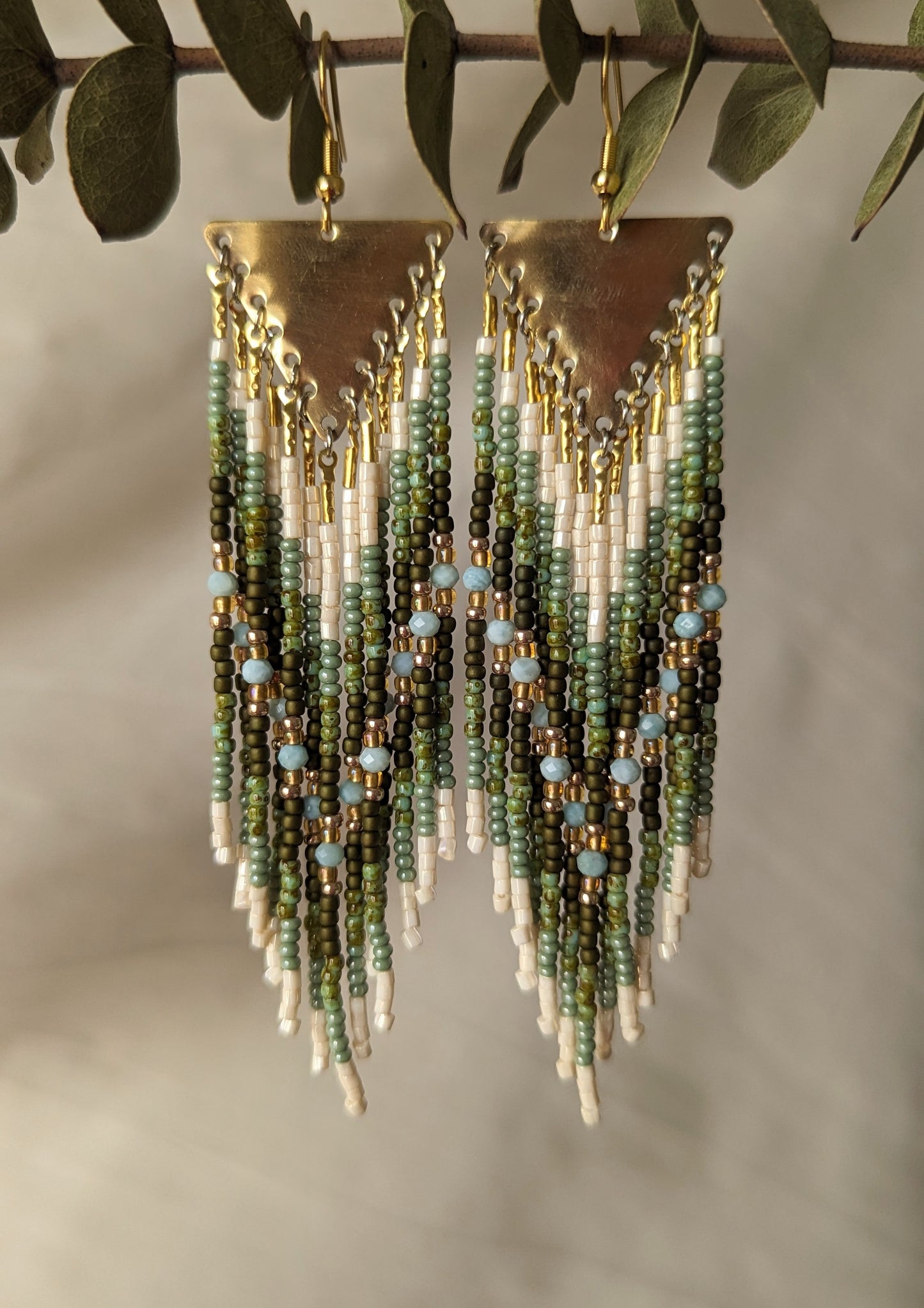 Moon & Milk green beaded earrings with ivory fringe and light blue stones, finished with brass triangles and inspired by earthy artisan beadwork.