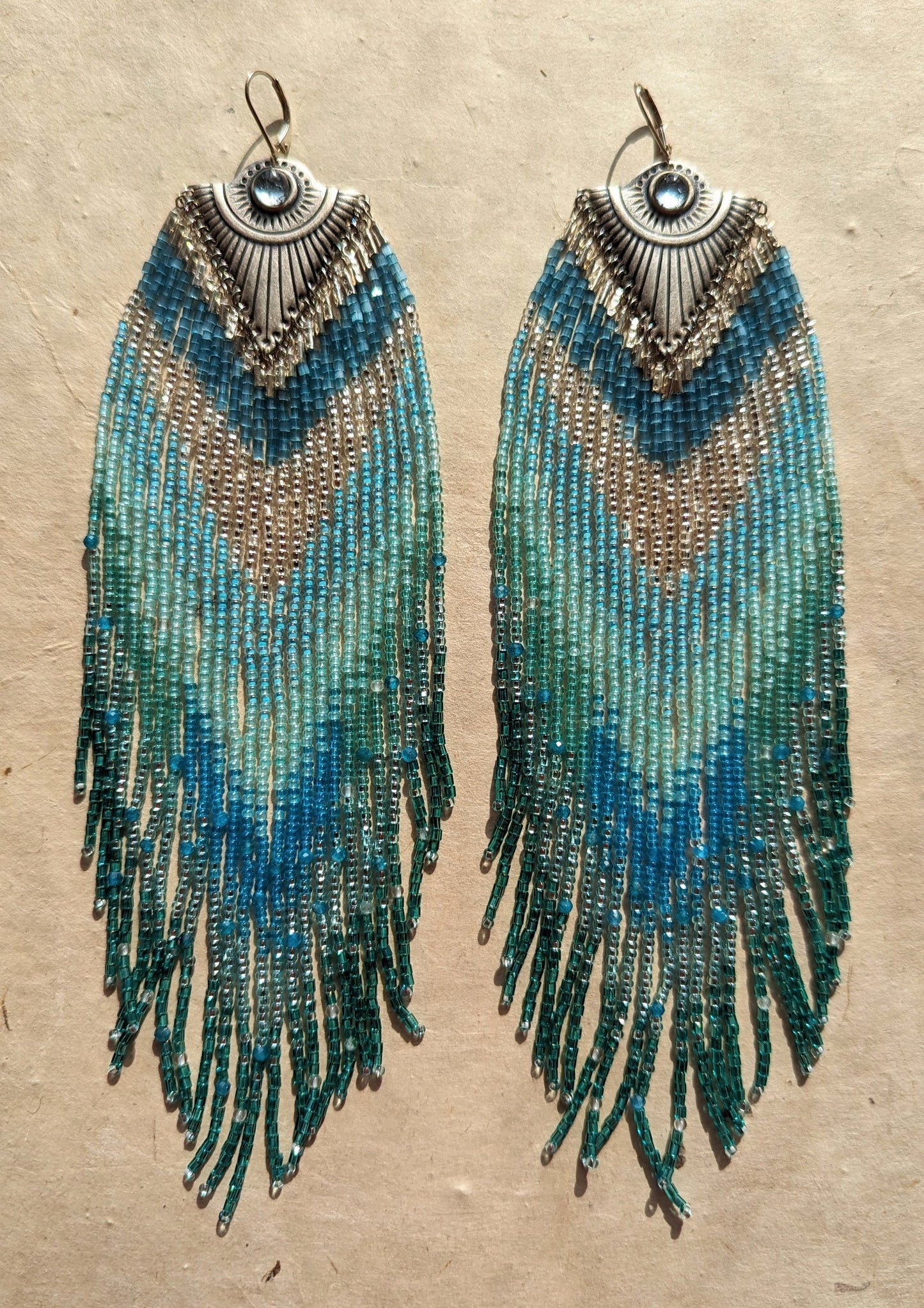 Moon & Milk - Handmade seed bead earrings featuring cascading blue and turquoise beads, accented with silver-tone pendants and central blue gemstones, elegantly displayed on a neutral background.