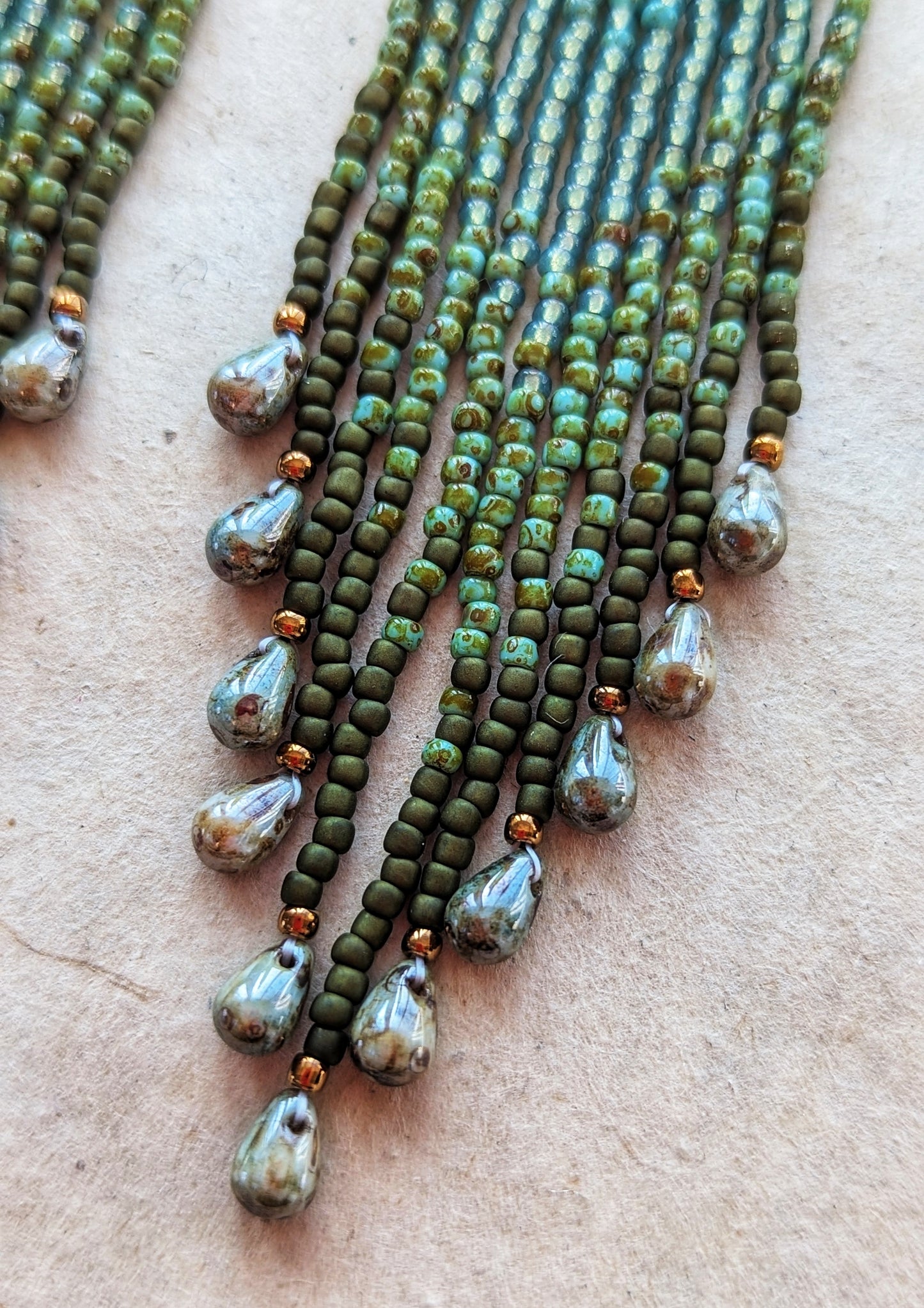 Close-up of long green ombré beaded earrings with teardrop ends, handcrafted to echo forest textures and artisan beadwork style.