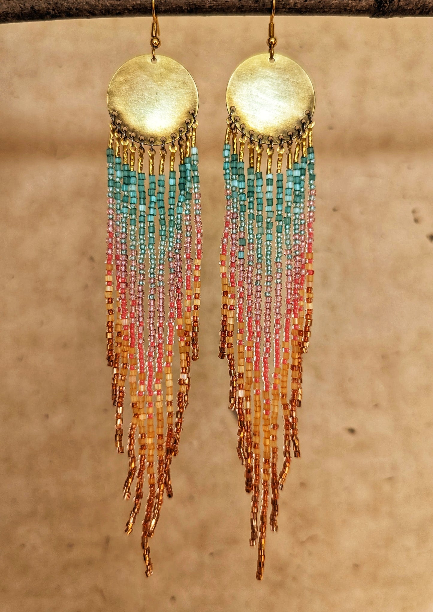 Handcrafted seed bead earrings with a vibrant ombre fringe design, transitioning from turquoise to pink to golden yellow, finished with copper-toned beads and a brass circular top.