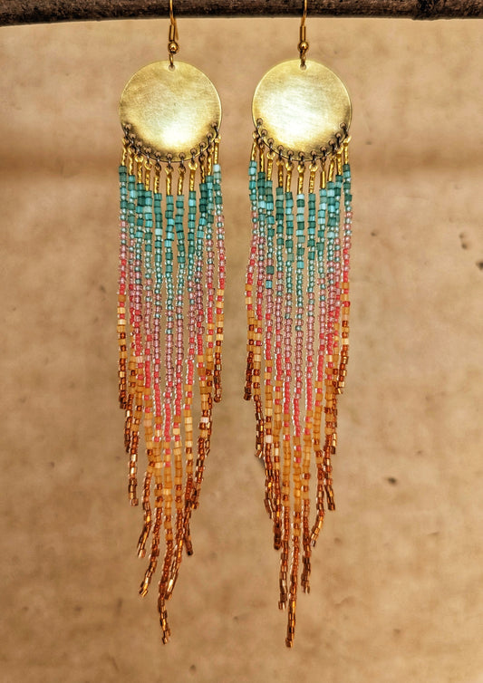 Handcrafted seed bead earrings with a vibrant ombre fringe design, transitioning from turquoise to pink to golden yellow, finished with copper-toned beads and a brass circular top.