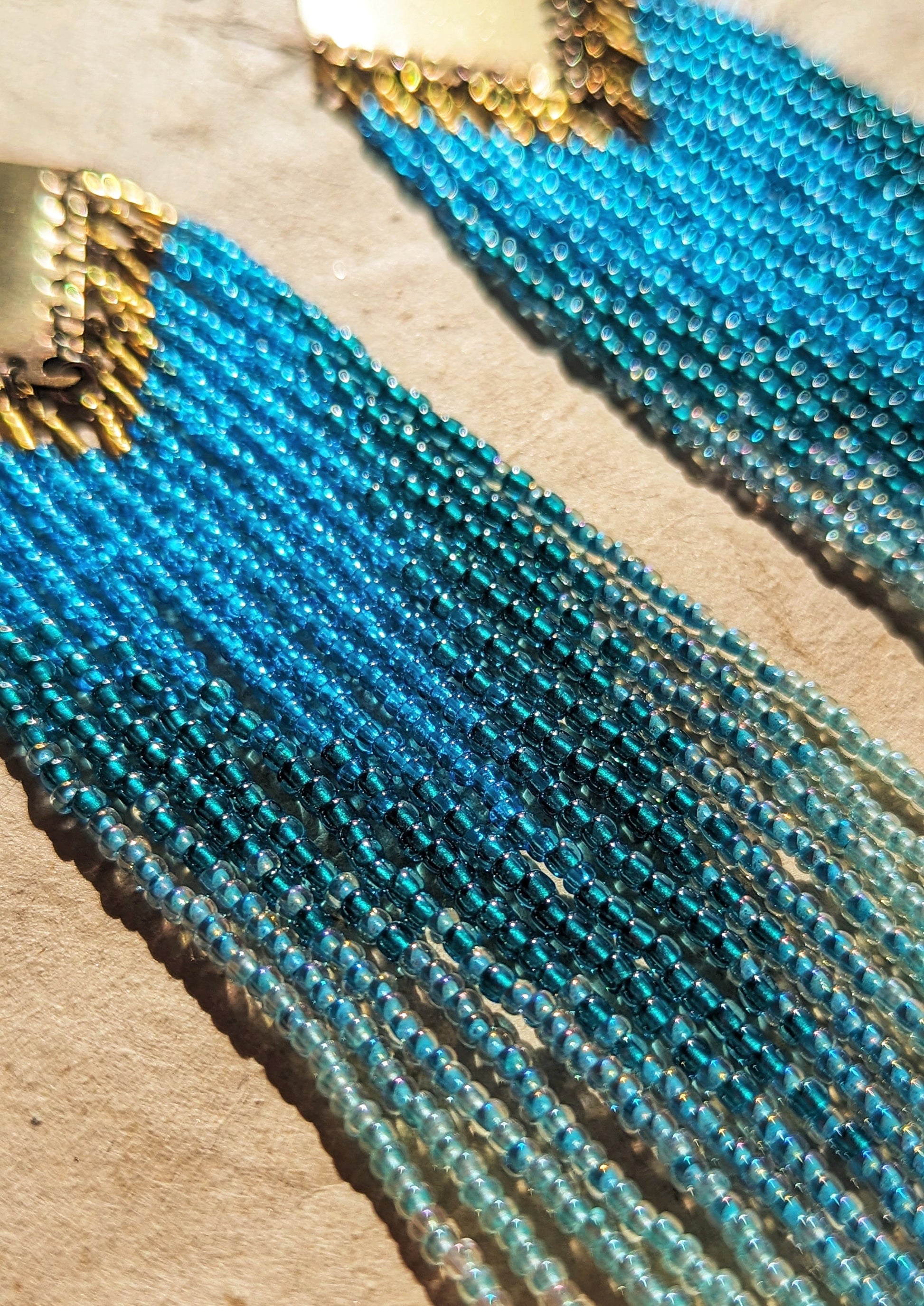 Close-up of long ombré blue and seafoam green beaded earrings by Moon & Milk, handmade with brass findings and inspired by Greek naiads and freshwater mysticism