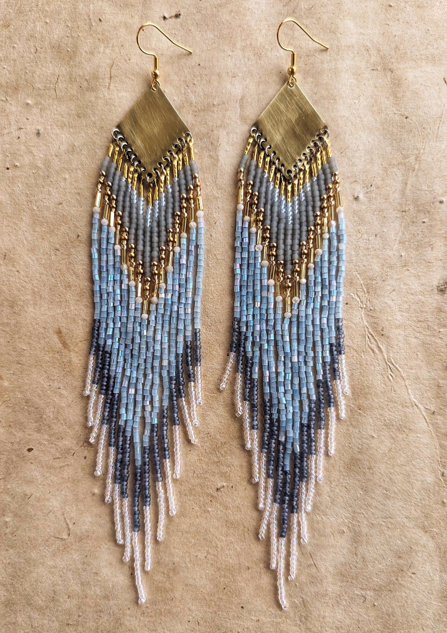 Moon & Milk beaded earrings inspired by Greek naiad Kyrene, featuring grey, pearl, and blue tones with long fringe on handcrafted brass triangles.