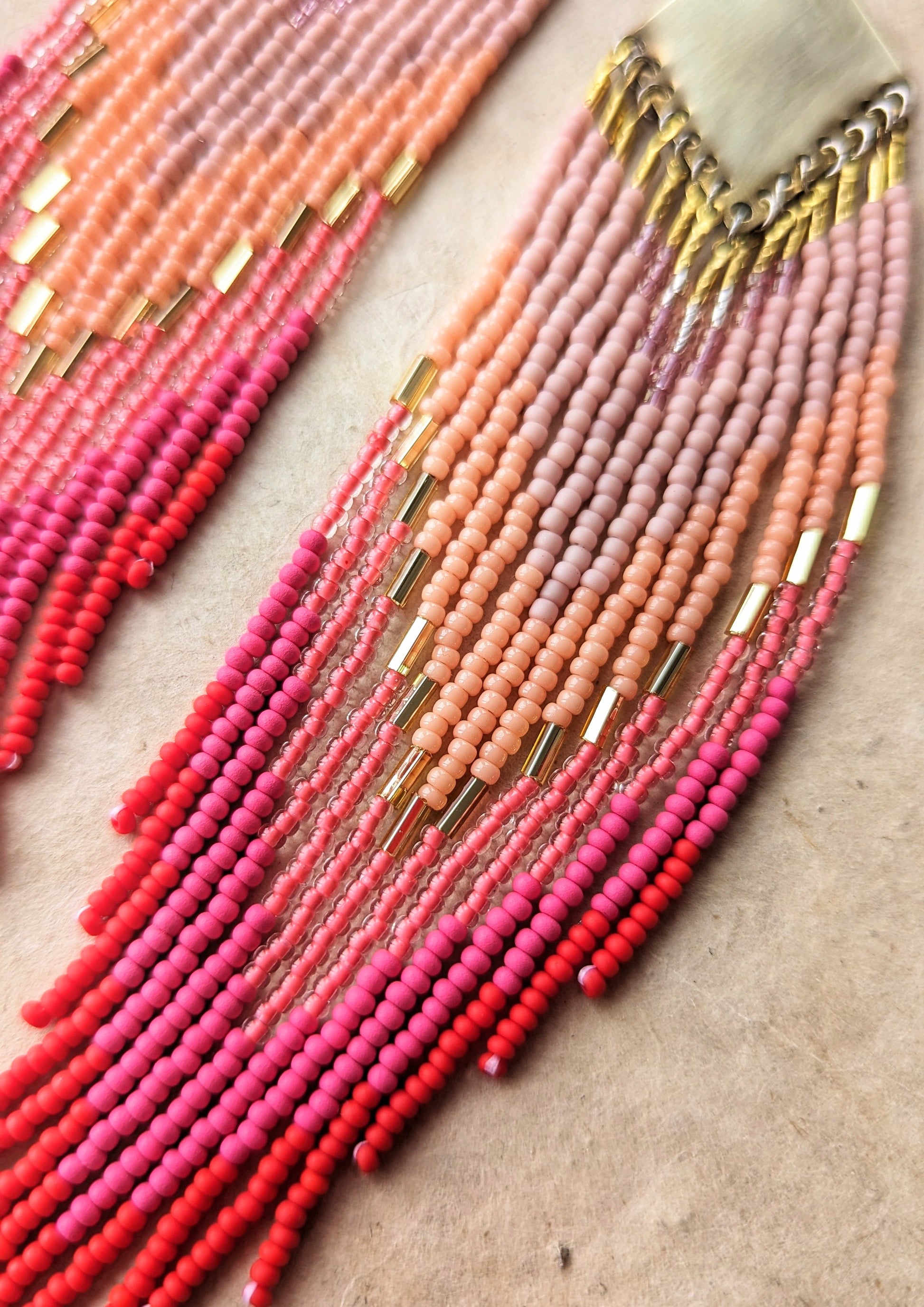 Moon & Milk handcrafted beaded earrings in ombré shades of rose, coral, and red with brass findings, displayed beside a dried pink rose on linen.