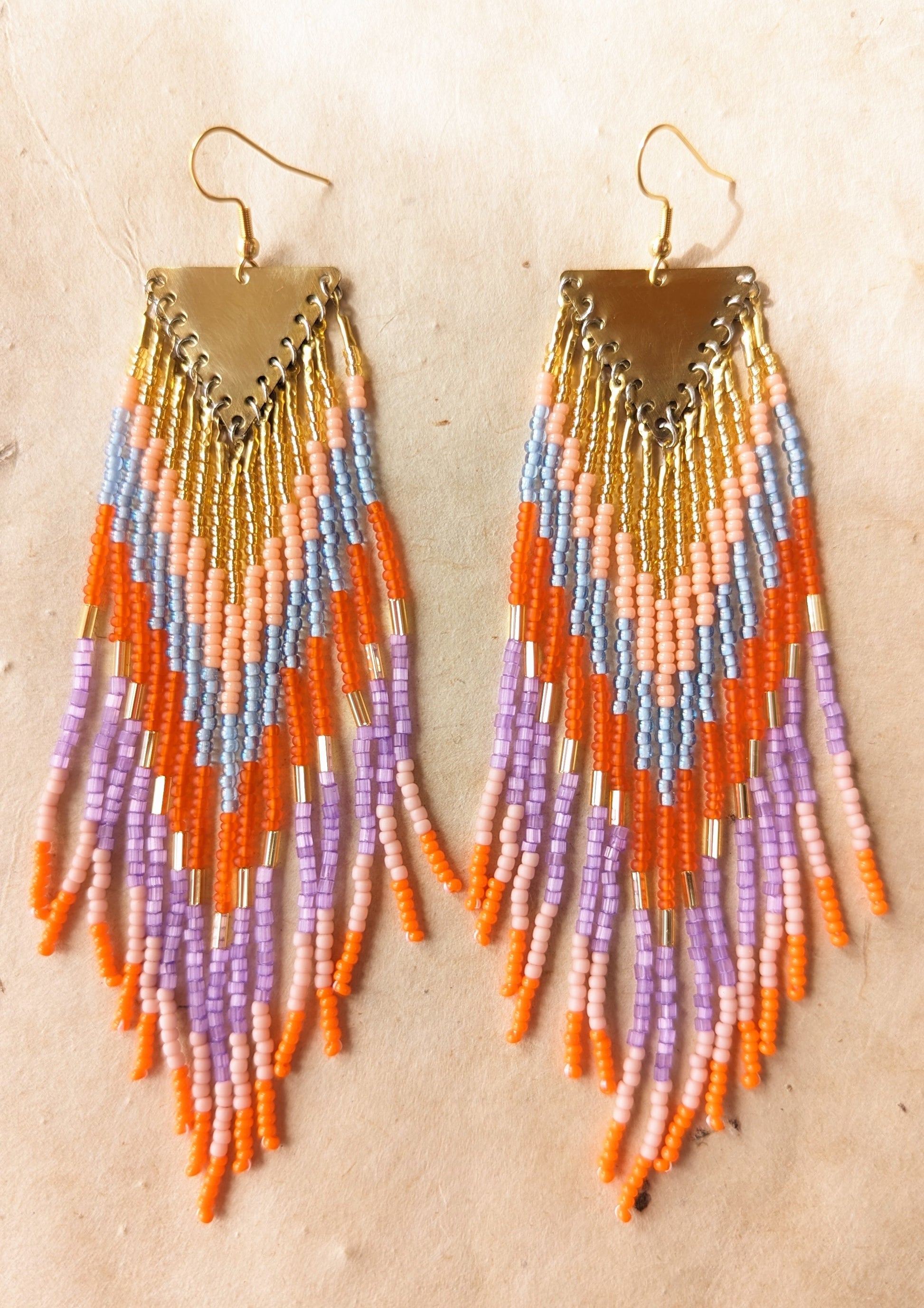 Colorful seed bead earrings with shades of orange, pink, purple,  gold, and light blue arranged in a triangular design, hanging from a brass finding.