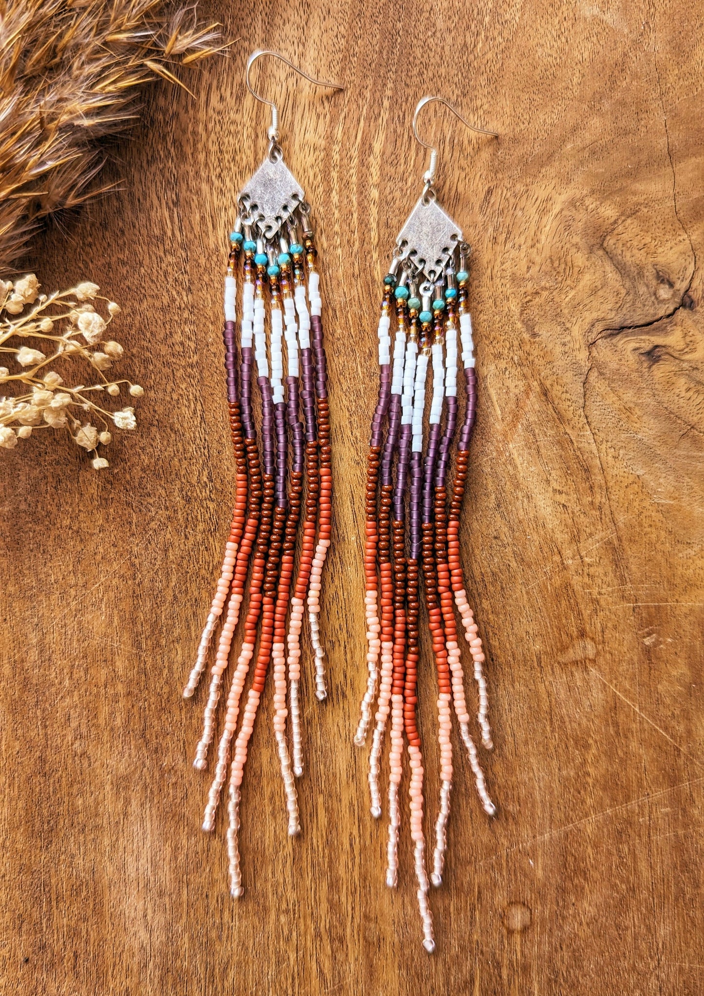 Long beaded fringe earrings with earthy tones of brown, terracotta, and white, displayed on a wooden background with dried floral accents.-Moon & Milk