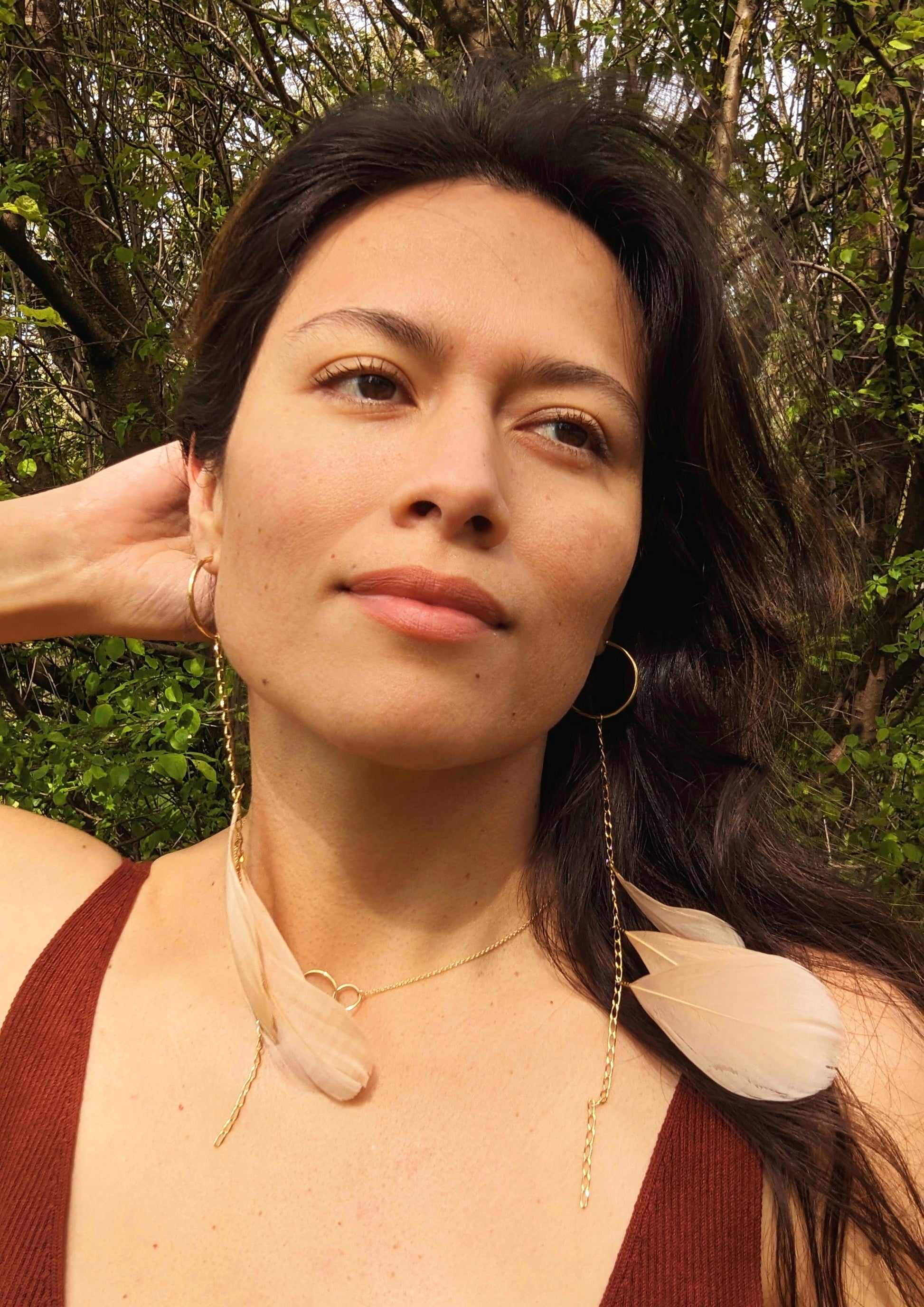Model wearing long blush feather earrings with gold hoops and chain, Moon & Milk design, photographed outdoors in natural light.