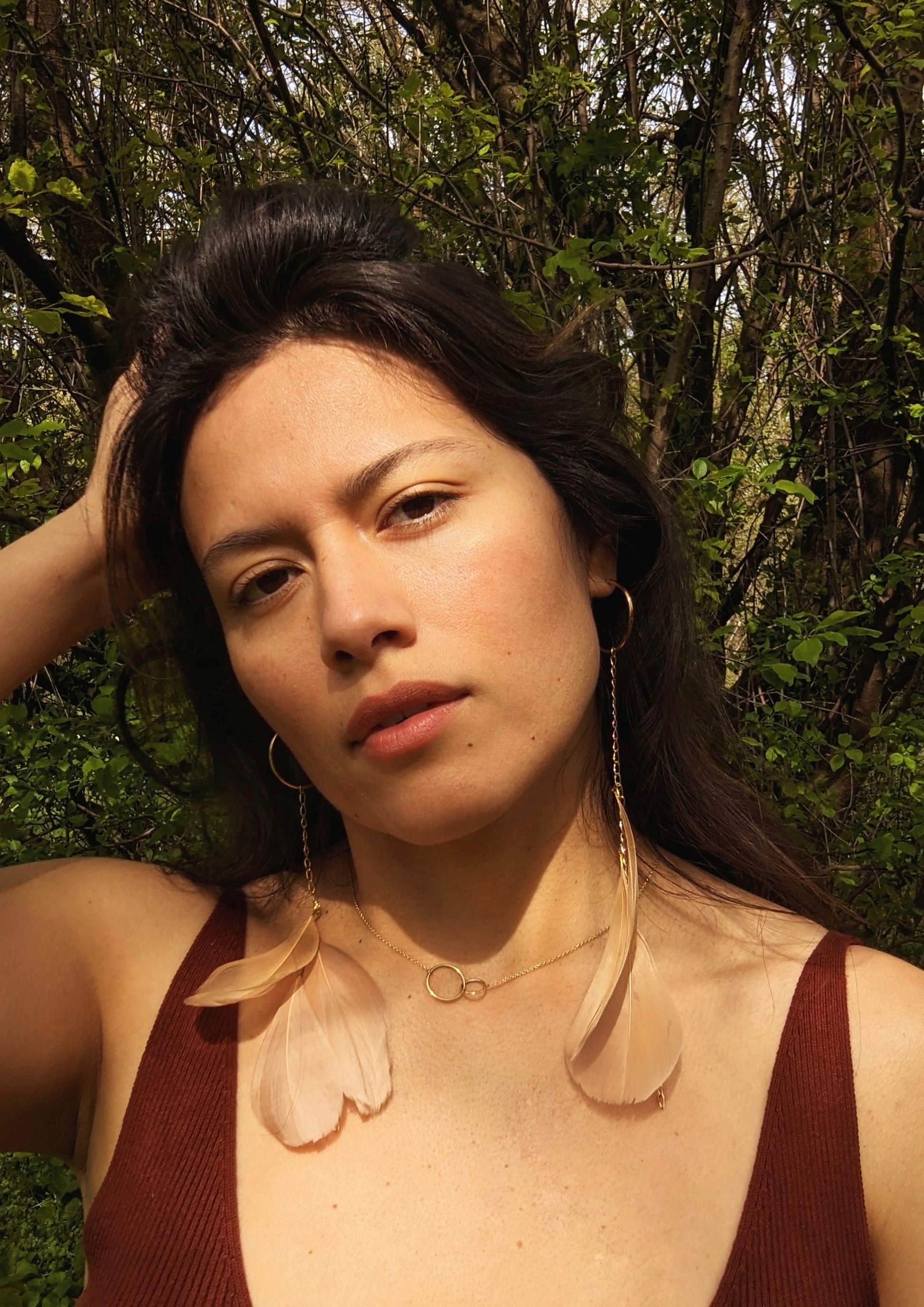 Model wearing long blush feather earrings with gold hoops and chain, Moon & Milk design, photographed outdoors in natural light.