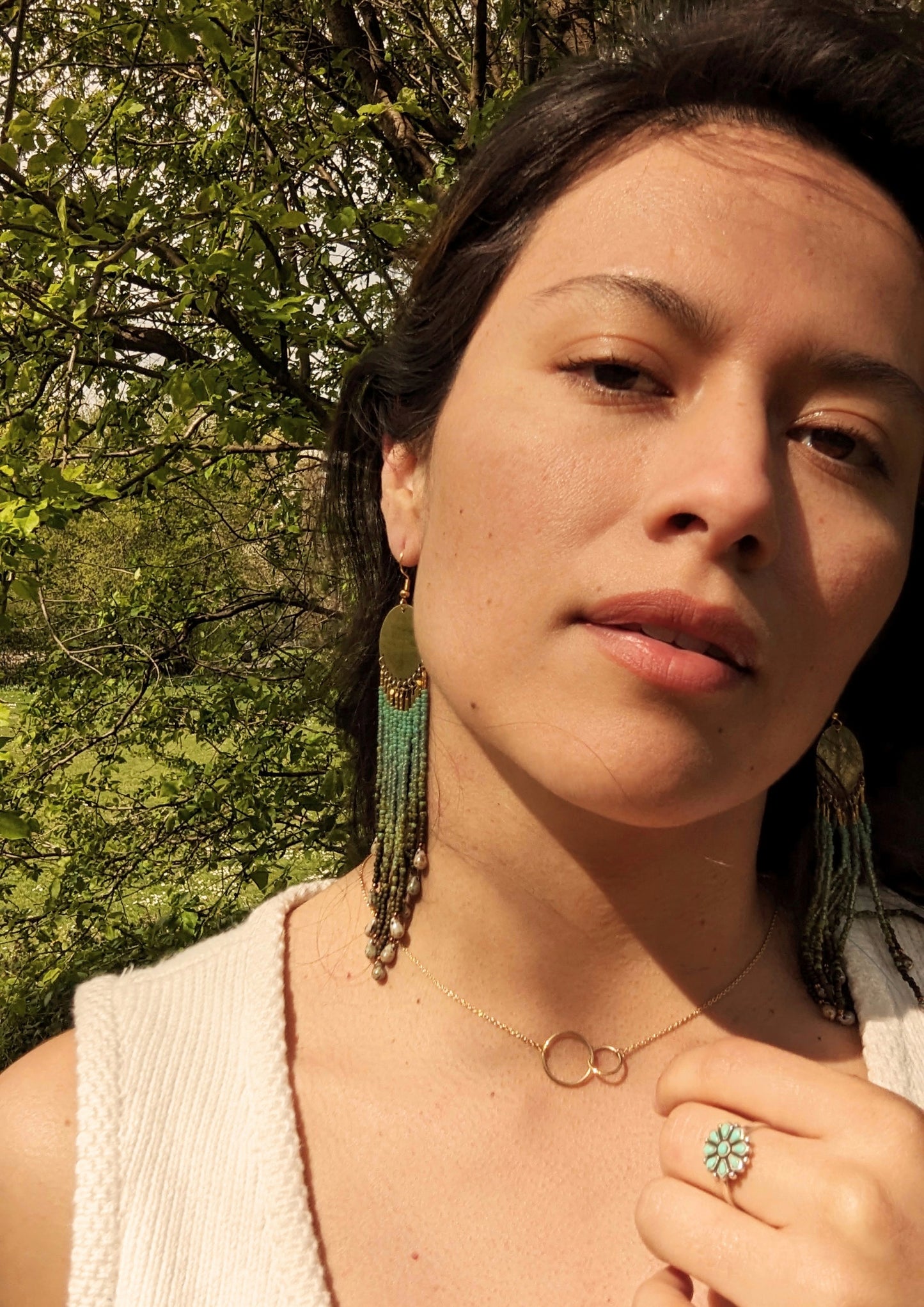 Woman wearing long green ombré beaded earrings with brass circles and teardrop ends, handcrafted to echo forest textures and artisan beadwork style.