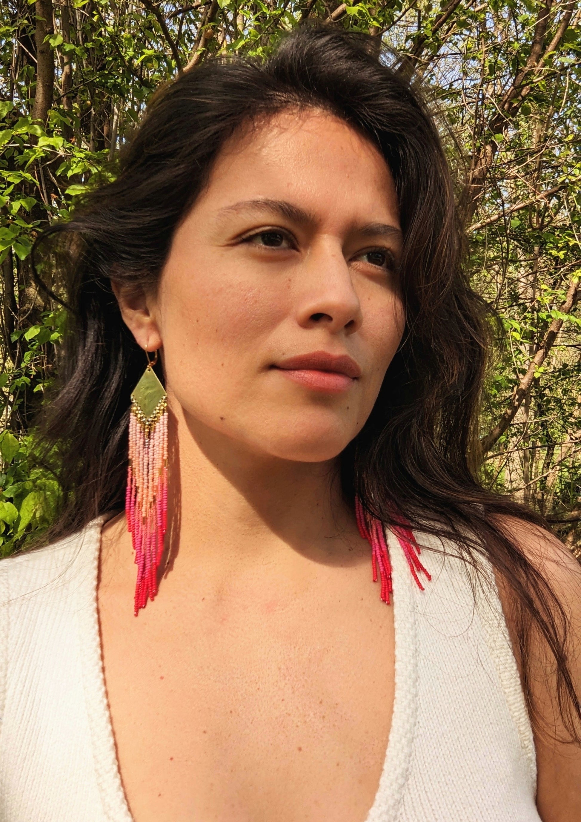 Moon & Milk handcrafted beaded earrings in ombré shades of rose, coral, and red with brass findings, worn by a woman.
