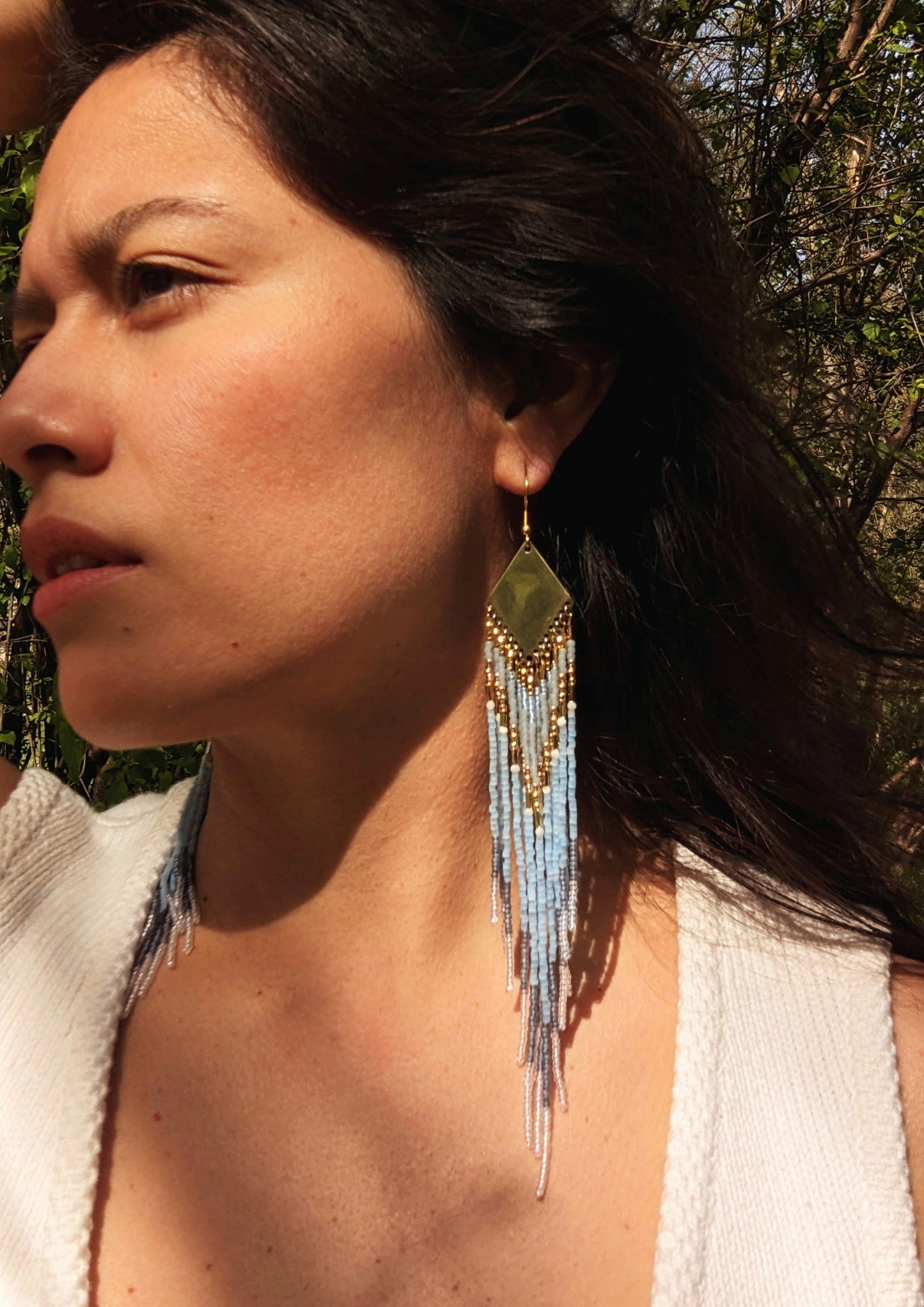 Moon & Milk beaded earrings inspired by Greek naiad Kyrene, featuring grey, pearl, and blue tones with long fringe on handcrafted brass triangles.