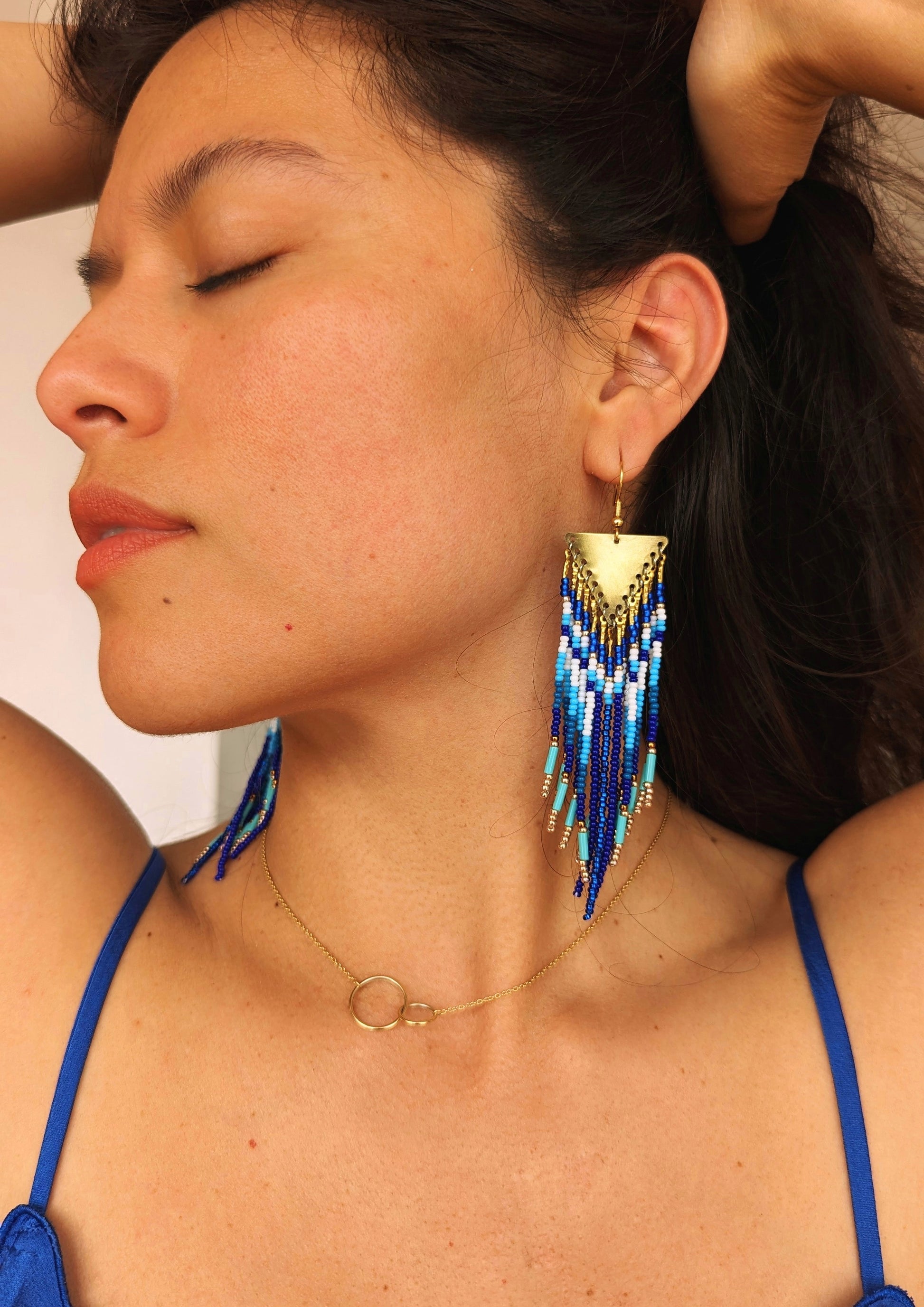 Woman wearing handcrafted  native earrings with cobalt, turquoise, and white beadwork, brass findings, and fringe design. Inspired by Utah landscapes.