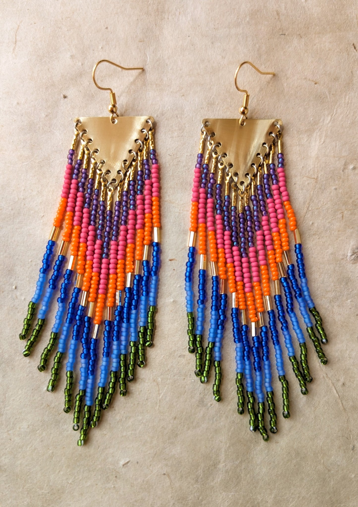 Moon & Milk Amazon-inspired beaded earrings featuring bold green, blue, pink, orange, and brass fringe with triangle brass tops.