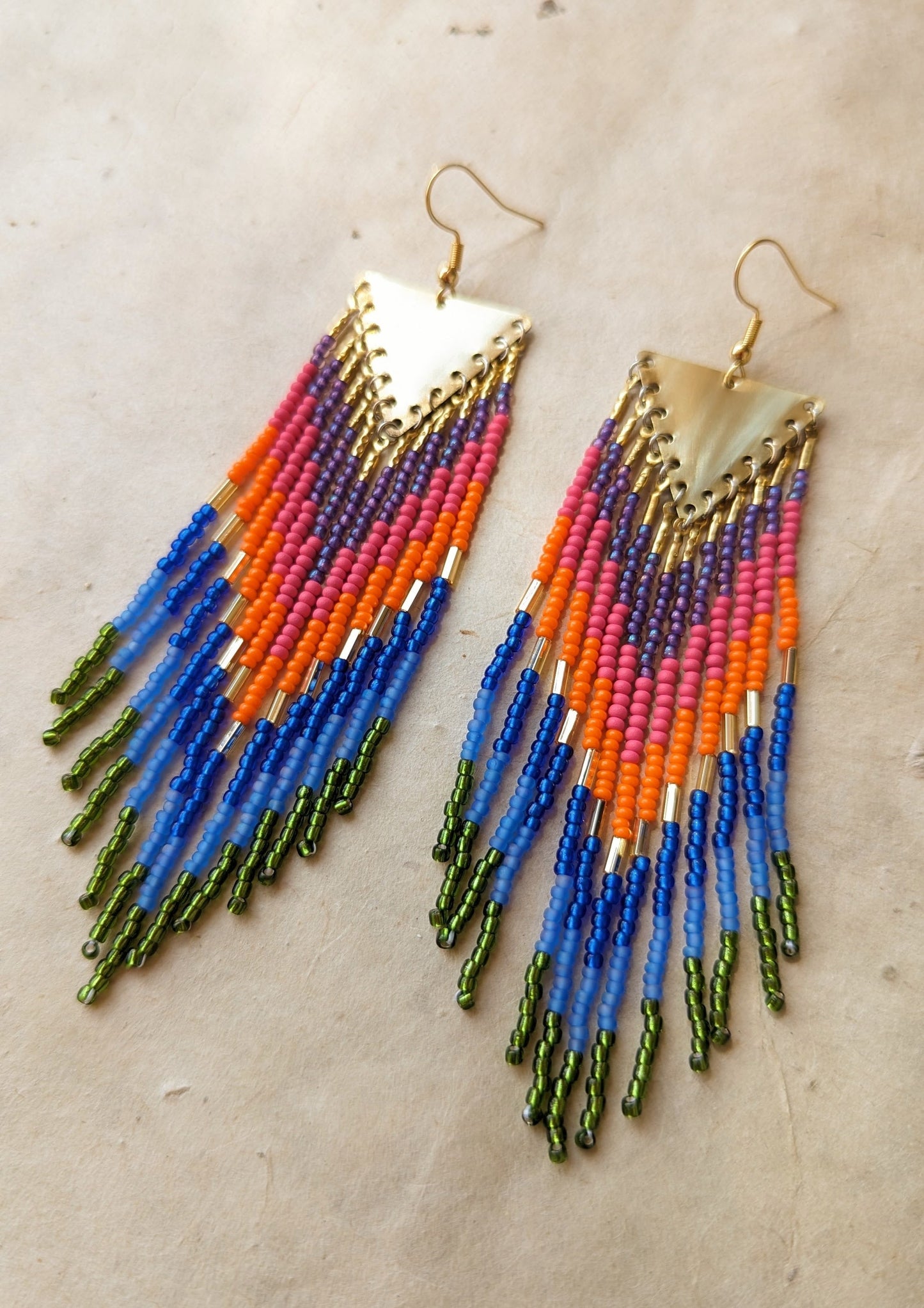 Moon & Milk Amazon-inspired beaded earrings featuring bold green, blue, pink, orange, and brass fringe with triangle brass tops.
