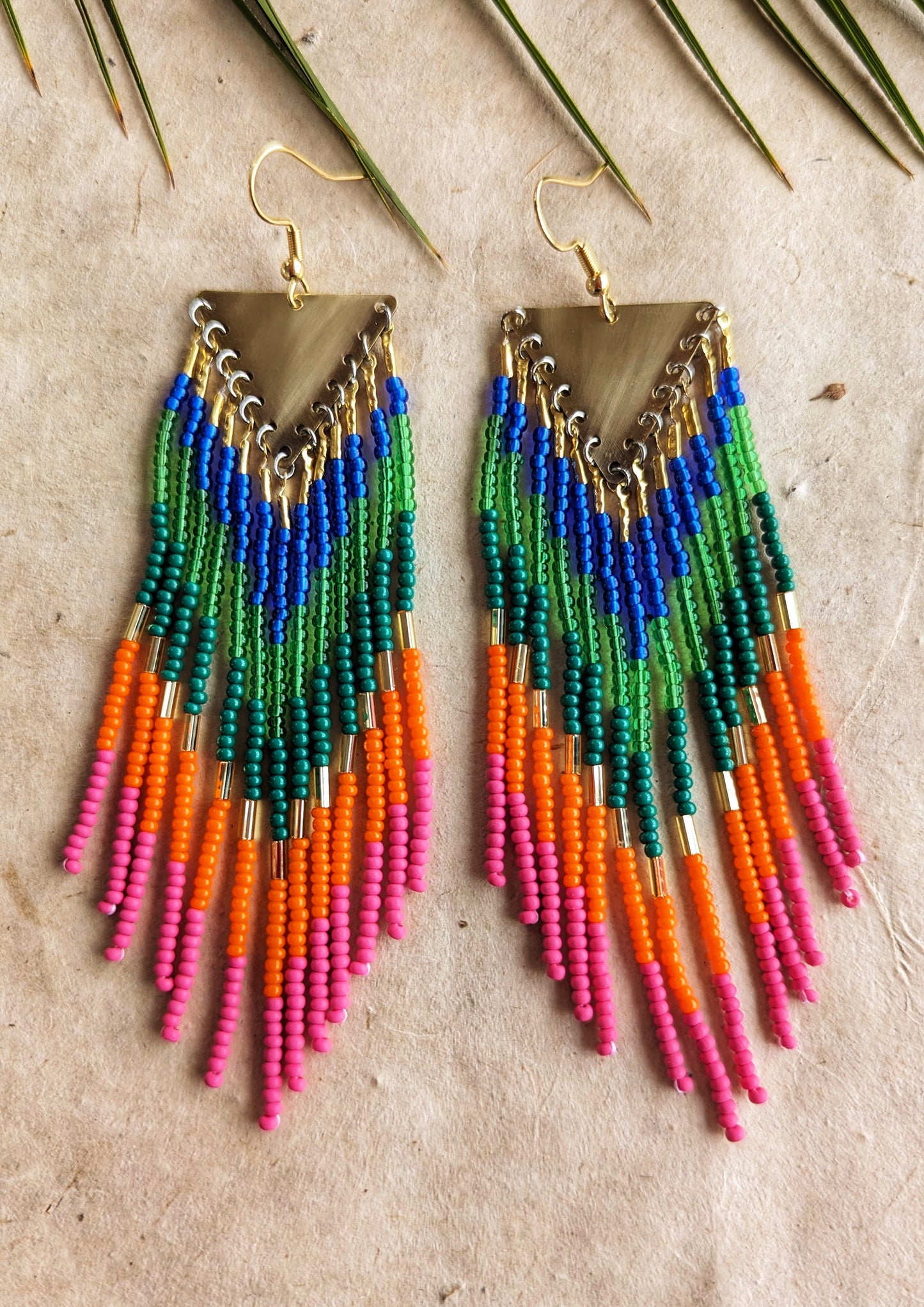 Colorful long beaded earrings with brass triangle tops and vibrant fringe in blue, green, orange, and pink seed beads arranged in a chevron pattern by Moon Milk.