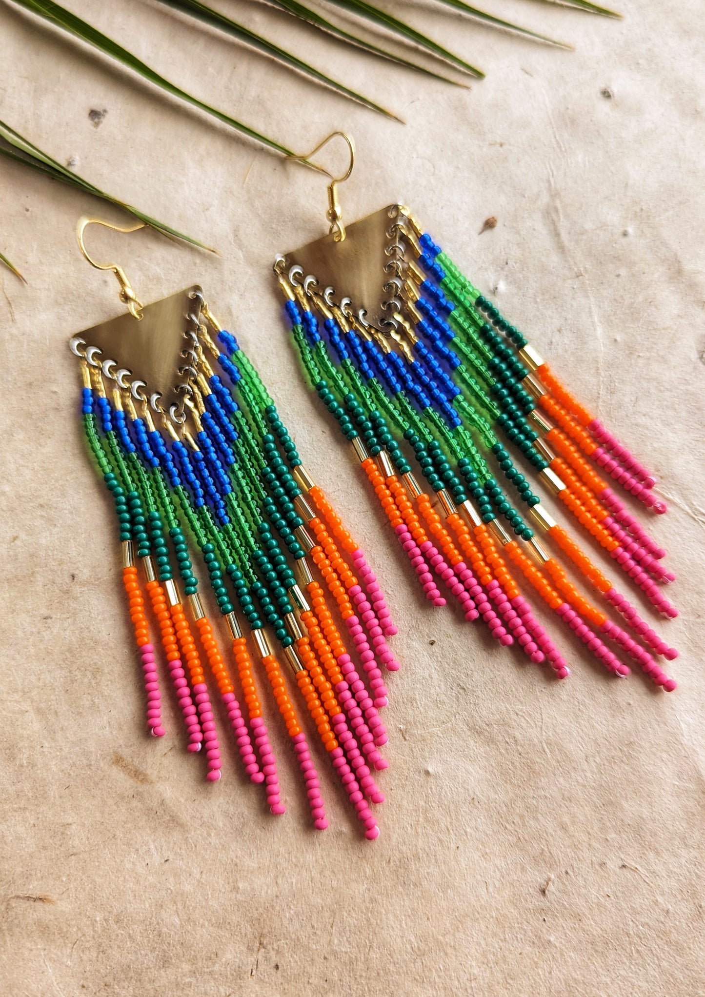 Colorful long beaded earrings with brass triangle tops and vibrant fringe in blue, green, orange, and pink seed beads arranged in a chevron pattern by Moon Milk.