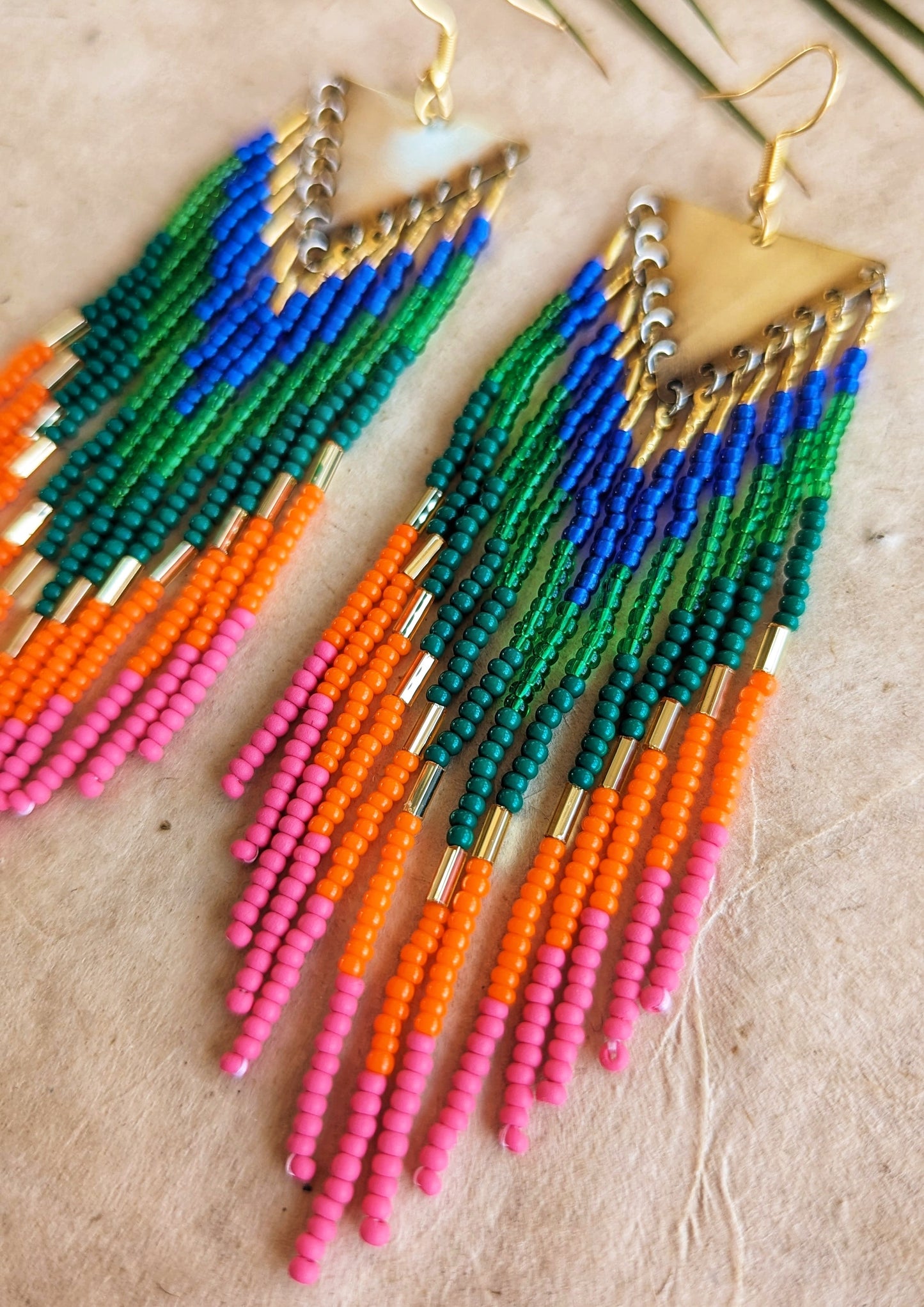 Colorful long beaded earrings with brass triangle tops and vibrant fringe in blue, green, orange, and pink seed beads arranged in a chevron pattern by Moon Milk.