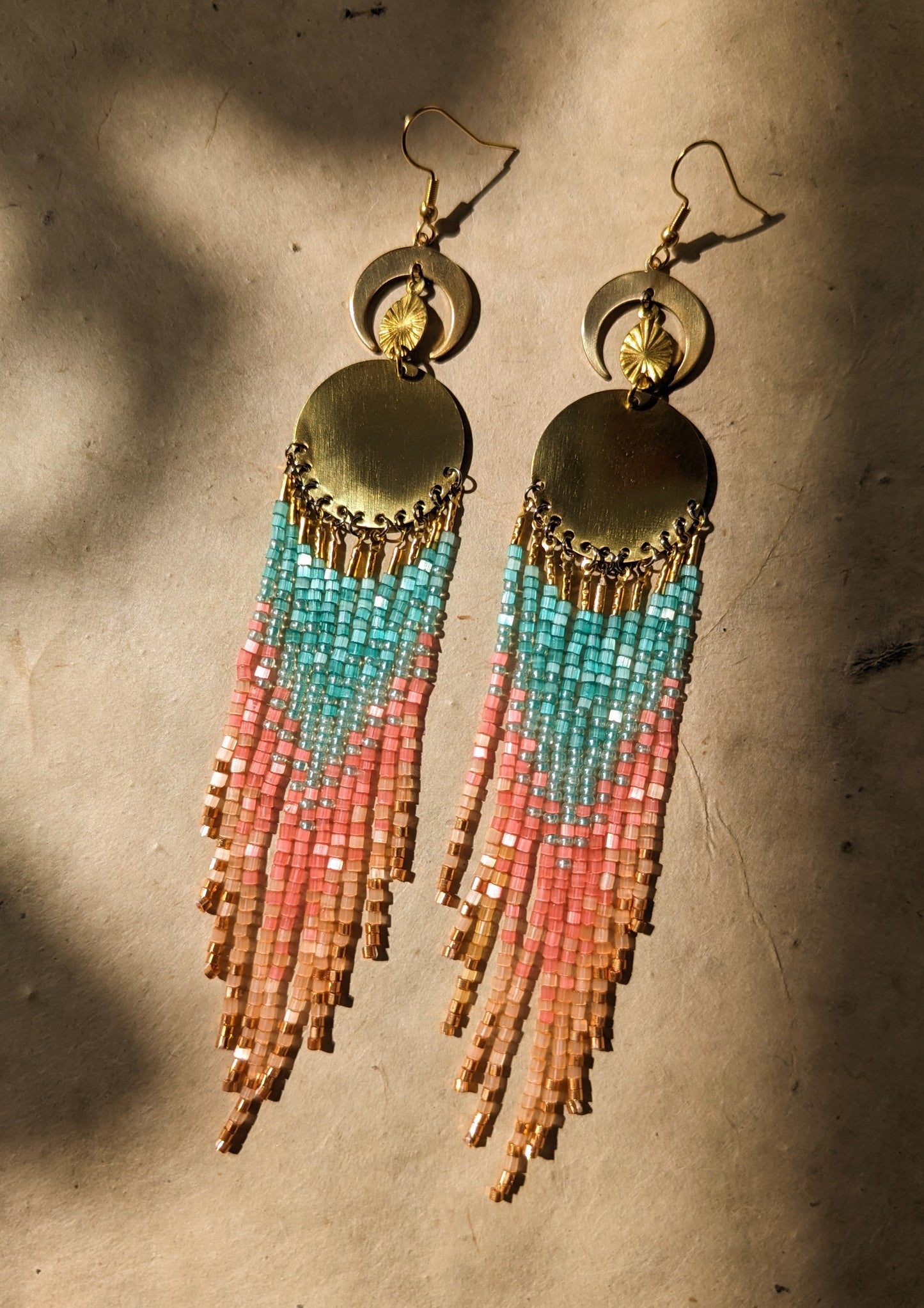 Seed bead earrings with turquoise, pink, and orange beaded strands in a gradient pattern, featuring crescent brass moon charms. - Moon & Milk