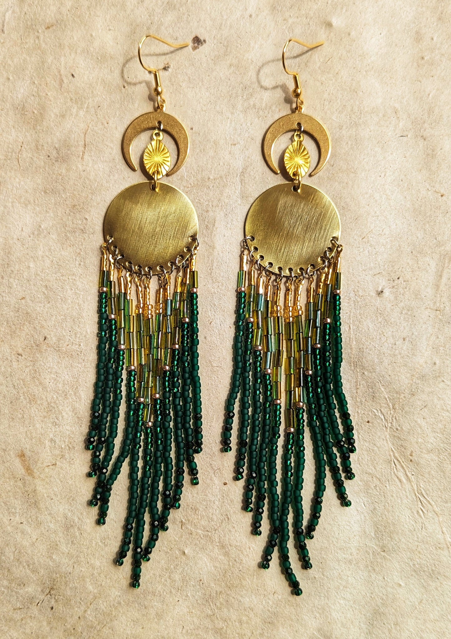 Brass statement earrings with green and gold beaded fringe, featuring a round centerpiece and crescent moon details. - Moon & Milk