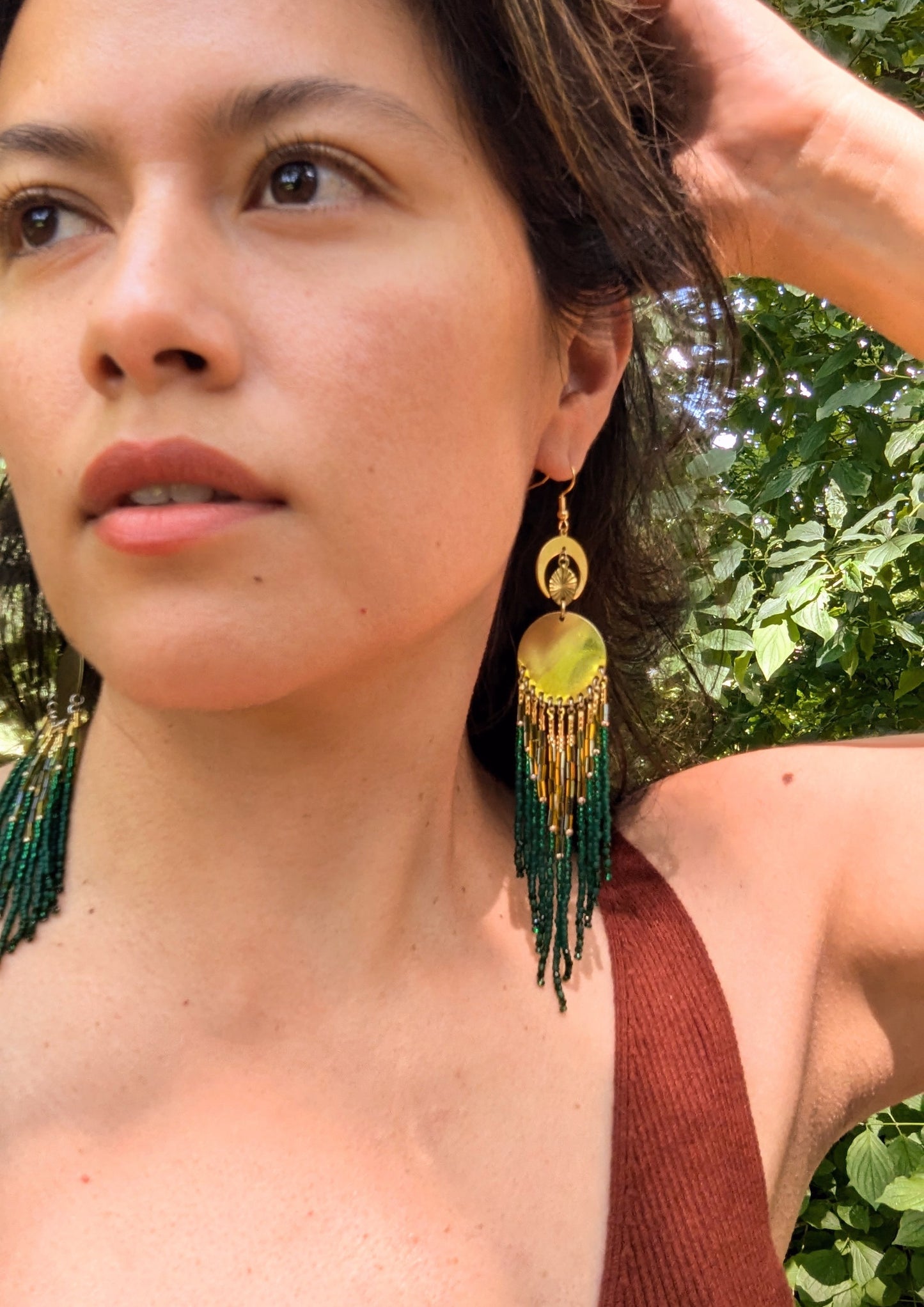 Model wearing brass and green beaded statement earrings with a crescent moon and circular design, standing out against a natural, outdoor background.- Moon & Milk