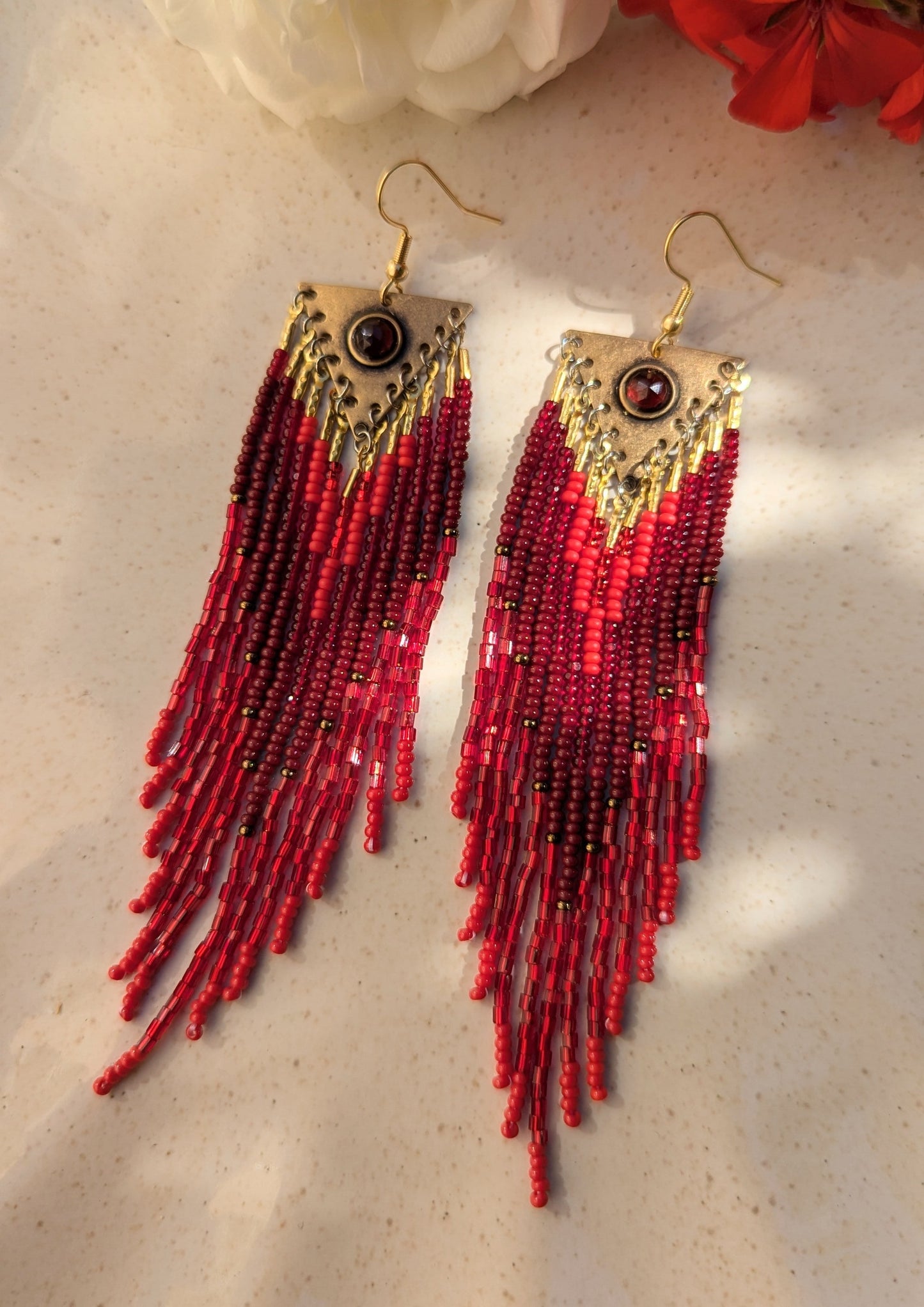 Handcrafted beaded earrings on by Moon & Milk, featuring red Czech beads, brass accents, and a garnet centerpiece, showcasing intricate beadwork and artistic design.