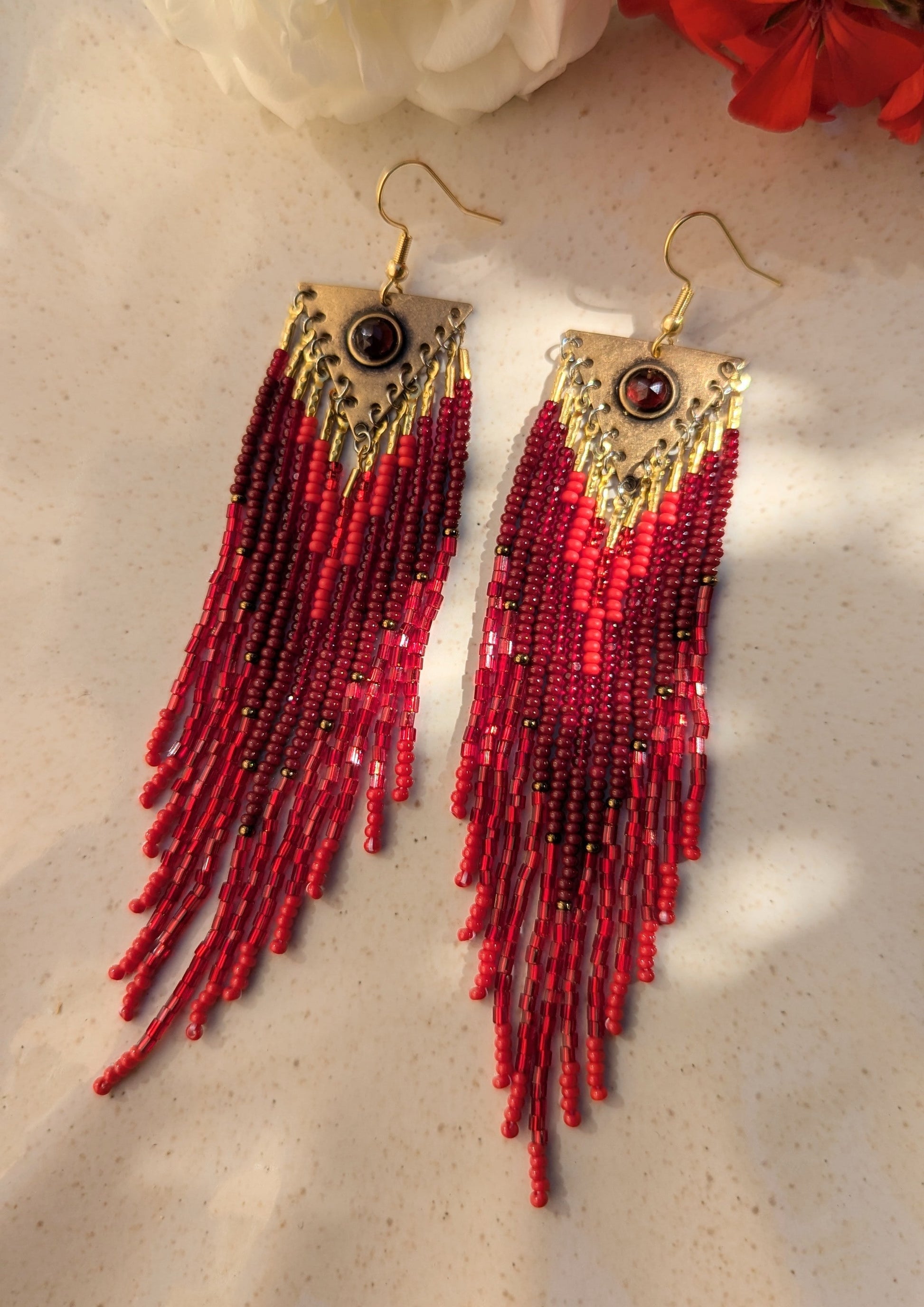 Handcrafted beaded earrings on by Moon & Milk, featuring red Czech beads, brass accents, and a garnet centerpiece, showcasing intricate beadwork and artistic design.