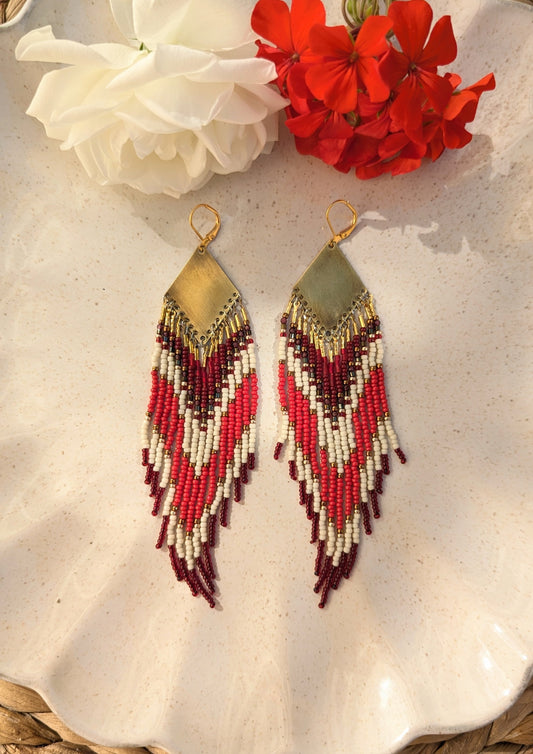 Moon & Milk handmade beaded earrings with burgundy, white, and red beadwork in chevron patterns hanging from brass diamond tops, displayed on a ceramic dish.