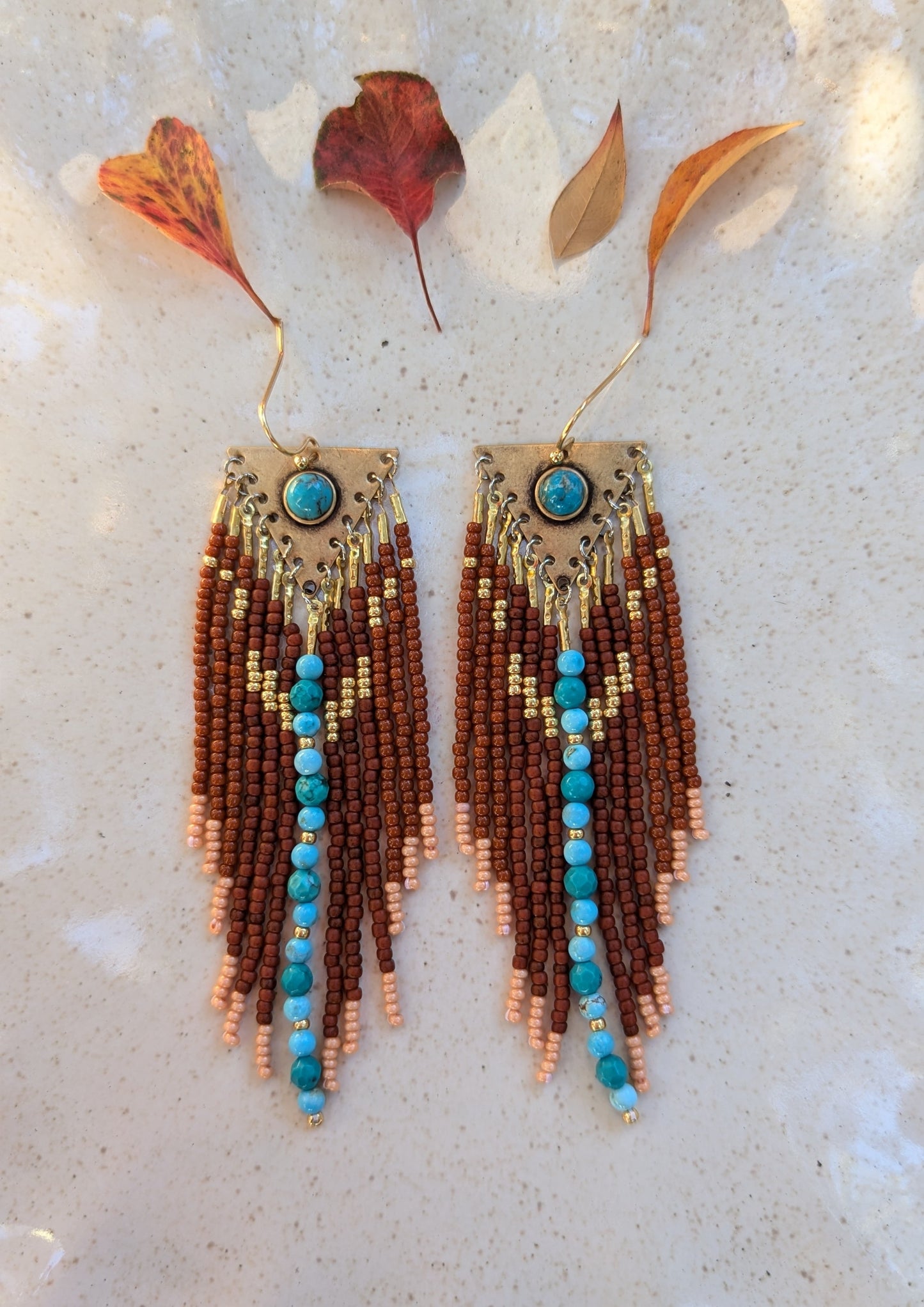 Handcrafted beaded earrings by Moon & Milk featuring rich brown glass beads, soft peach accents, and turquoise stones set in brass. Cascading fringes and vibrant beadwork create a Southwestern design.