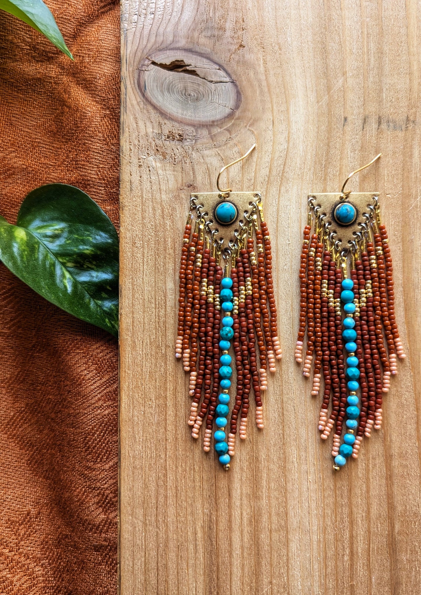 Handcrafted beaded earrings by Moon & Milk featuring rich brown glass beads, soft peach accents, and turquoise stones set in brass. Cascading fringes and vibrant beadwork create a Southwestern design.
