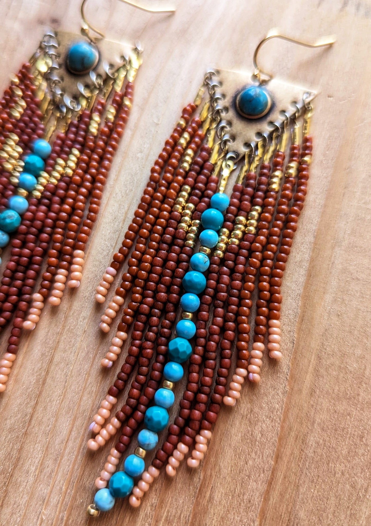 Handcrafted beaded earrings by Moon & Milk featuring rich brown glass beads, soft peach accents, and turquoise stones set in brass. Cascading fringes and vibrant beadwork create a Southwestern design.