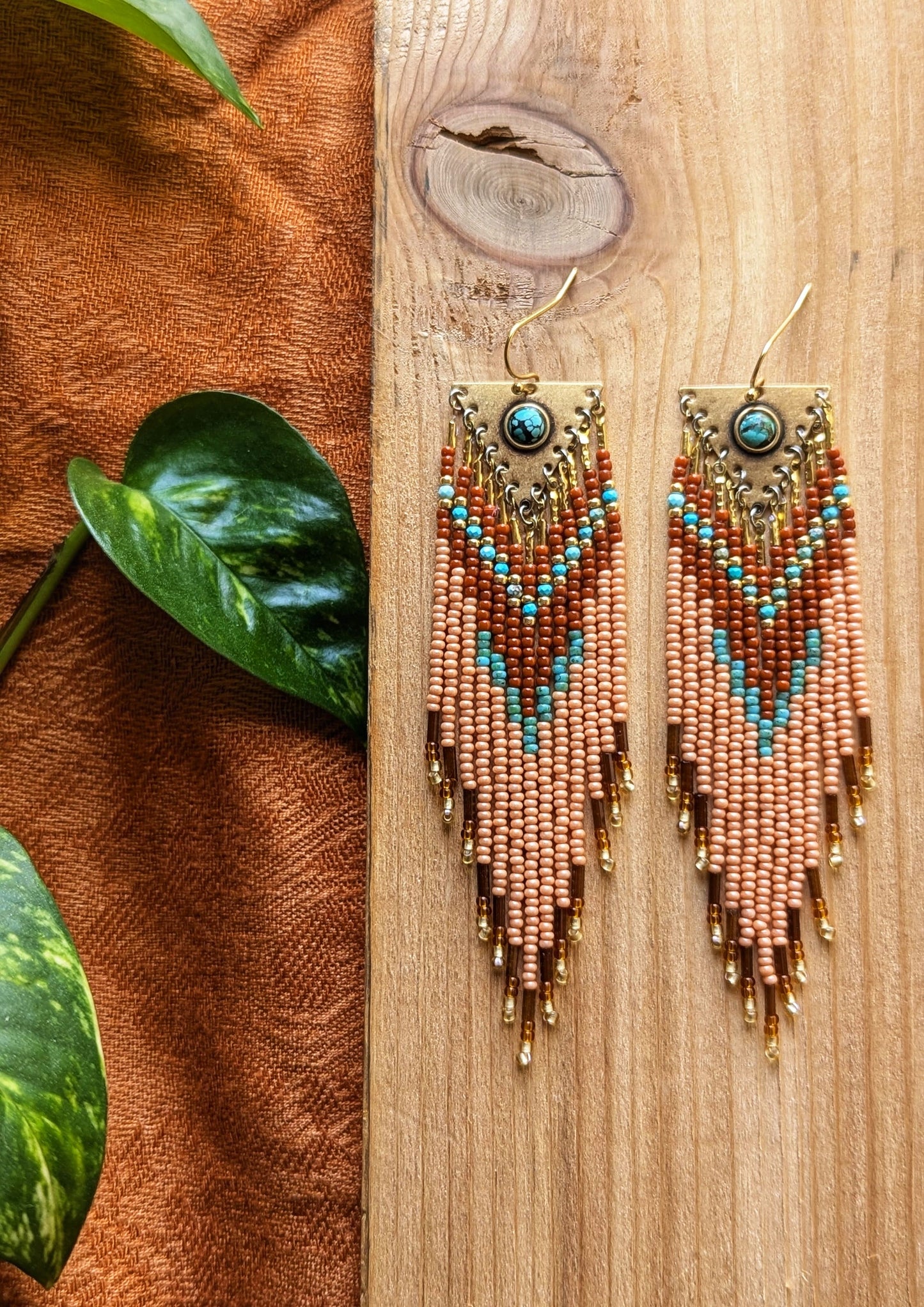 Long beaded earrings in burnt orange, peach, turquoise, and gold with brass charms, handmade with a warm fall color palette by Moon & Milk.