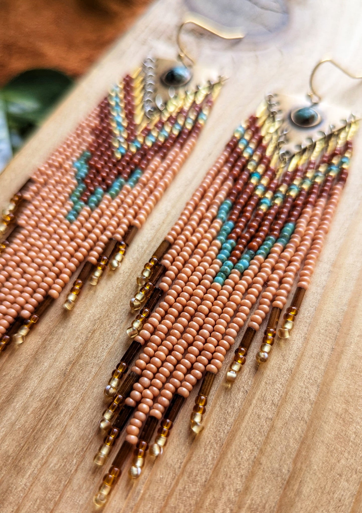 Long beaded earrings in burnt orange, peach, turquoise, and gold with brass charms, handmade with a warm fall color palette by Moon & Milk.