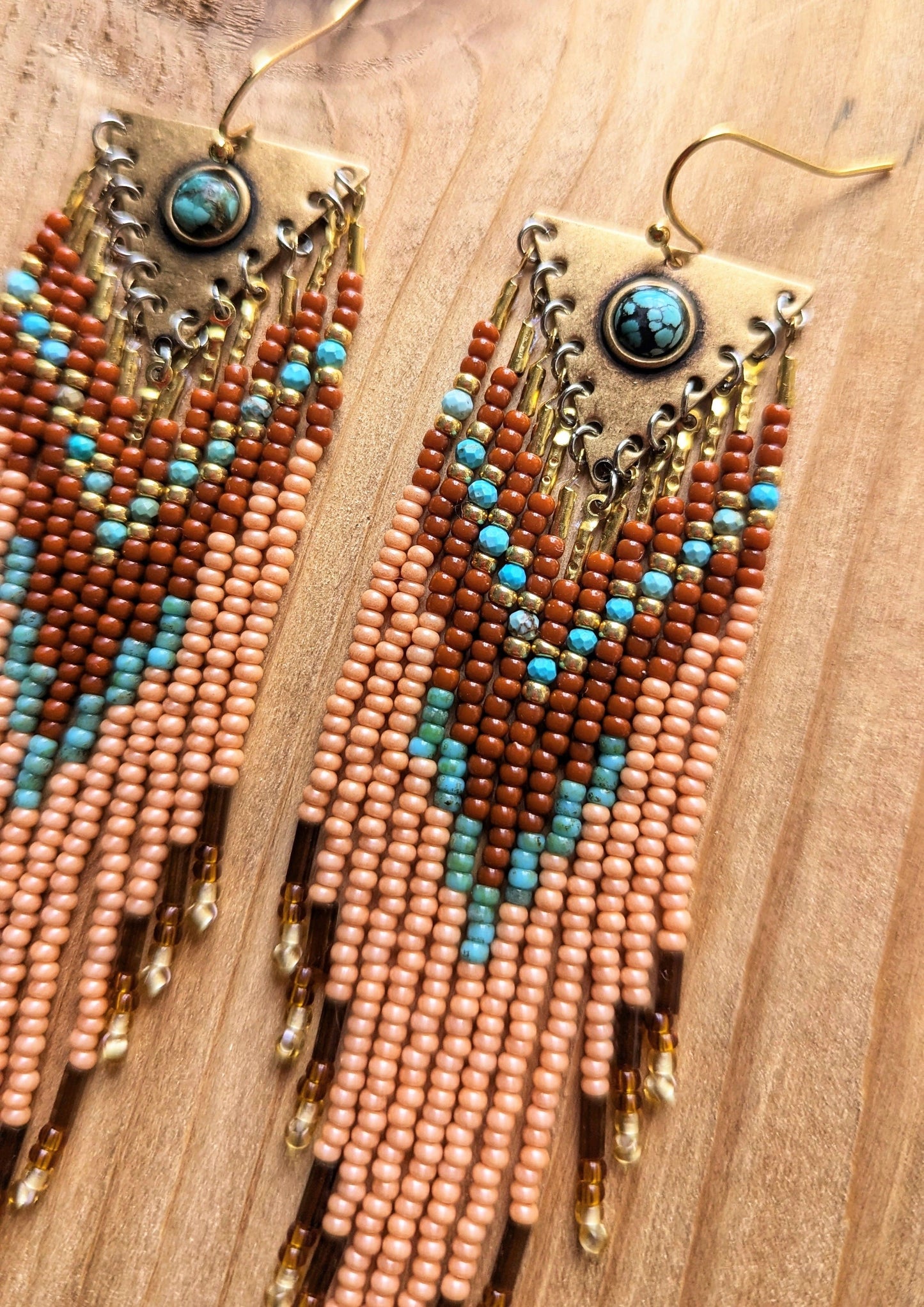 Long beaded earrings in burnt orange, peach, turquoise, and gold with brass charms, handmade with a warm fall color palette by Moon & Milk.