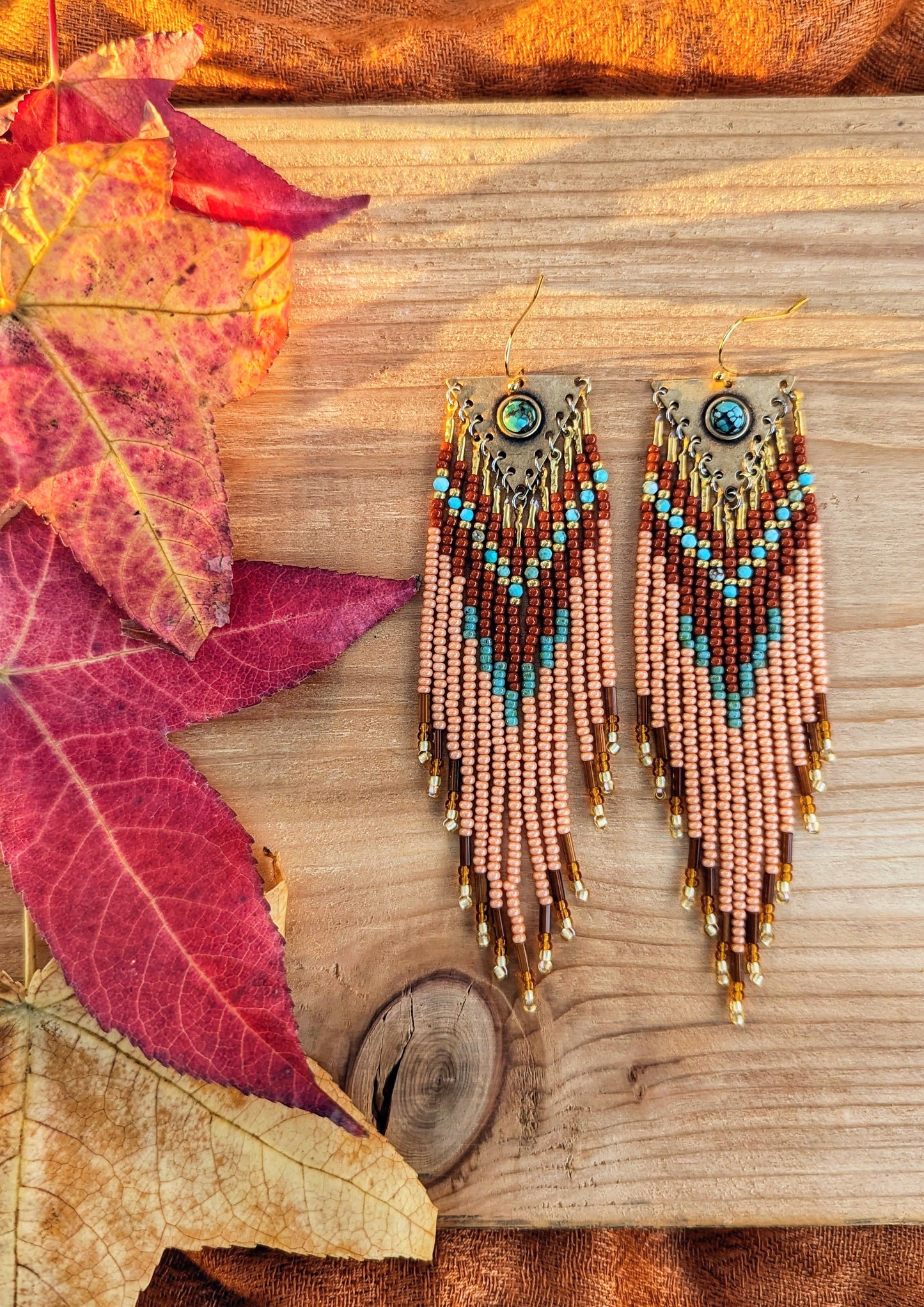 Long beaded earrings in burnt orange, peach, turquoise, and gold with brass charms, handmade with a warm fall color palette by Moon & Milk.