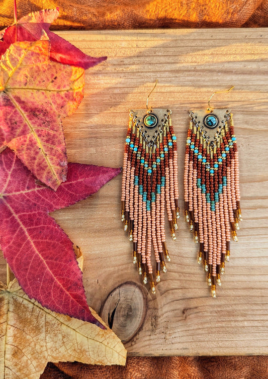 Long beaded earrings in burnt orange, peach, turquoise, and gold with brass charms, handmade with a warm fall color palette by Moon & Milk.