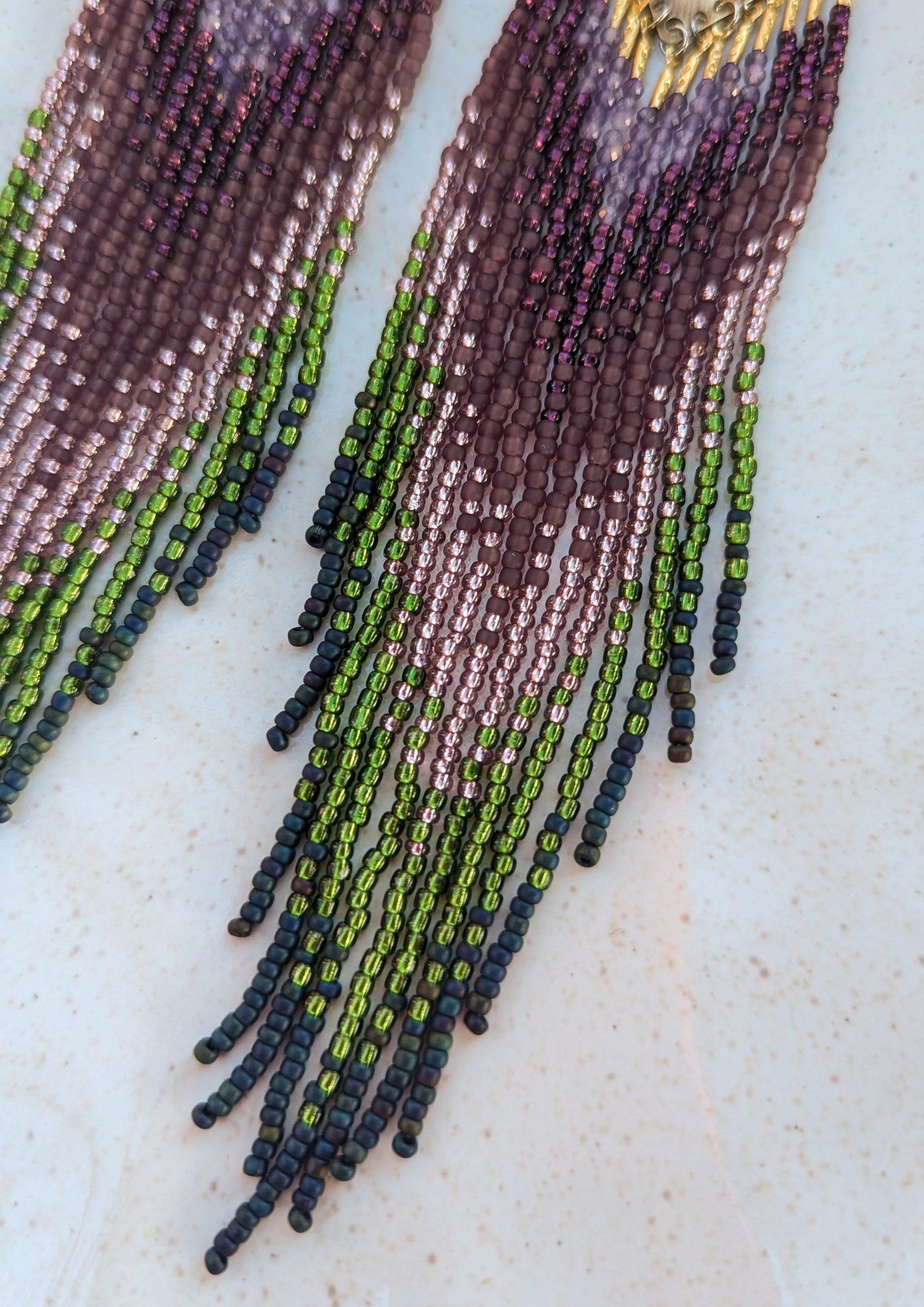 Moon & Milk handcrafted beaded earrings with purple, green, and navy glass beads, brass tops, and long fringe, designed as artisan wearable art.