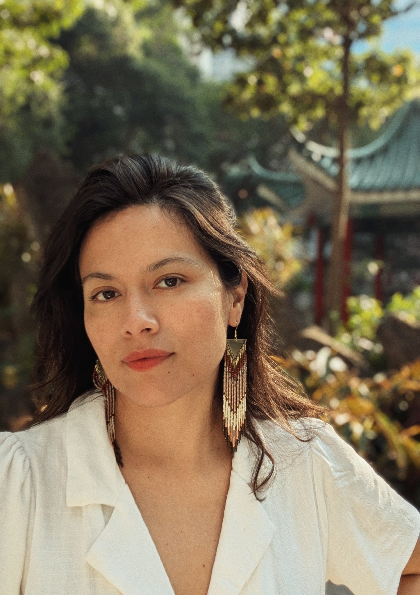 Long handcrafted fringe earrings by Moon & Milk with warm terracotta, beige, and ivory seed beads, finished with brass triangle tops and fine detailing worn by a woman.