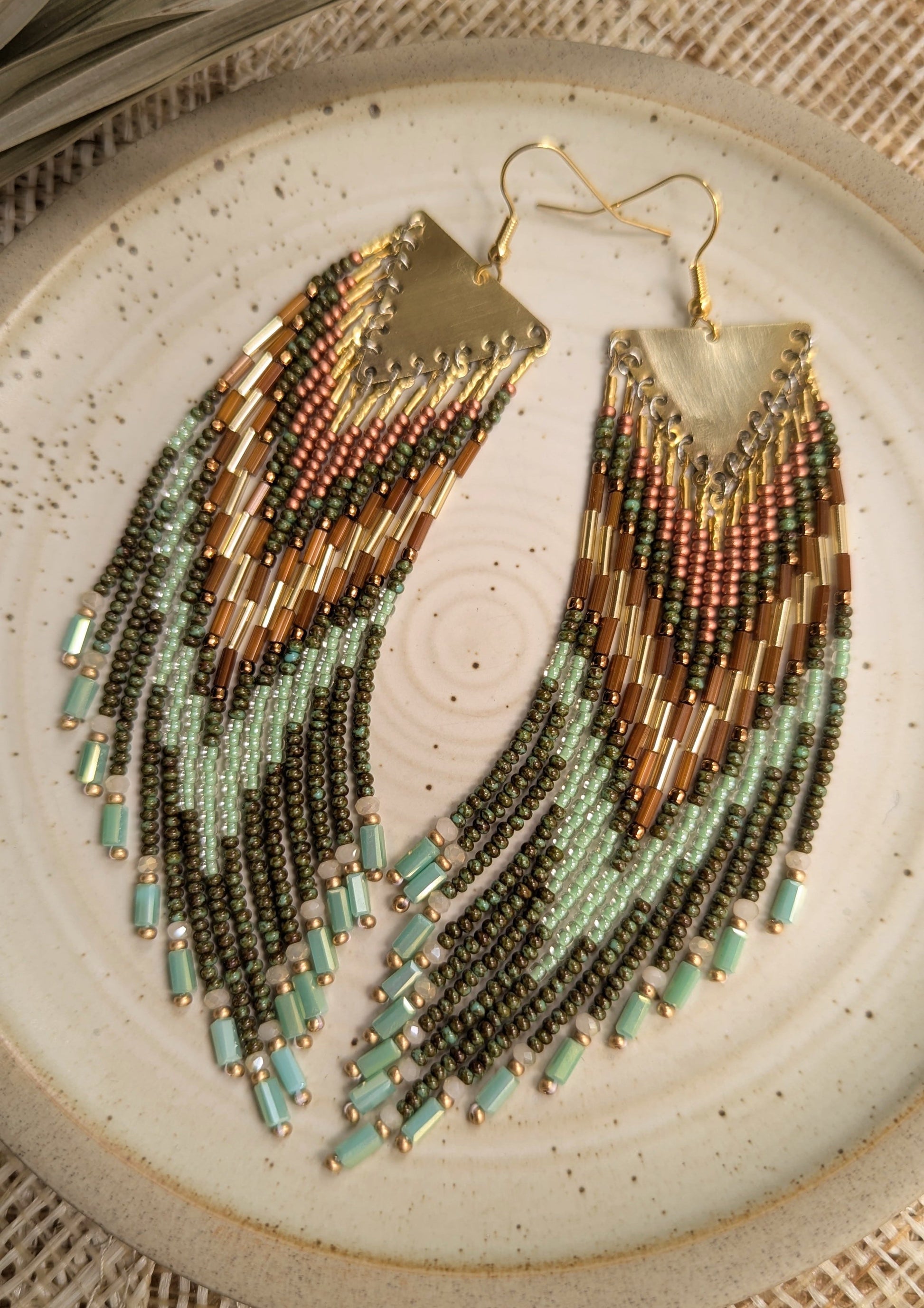 Moon & Milk handcrafted fringe earrings with olive green, mint, and bronze seed beads and brass findings, displayed on a ceramic plate in natural light.